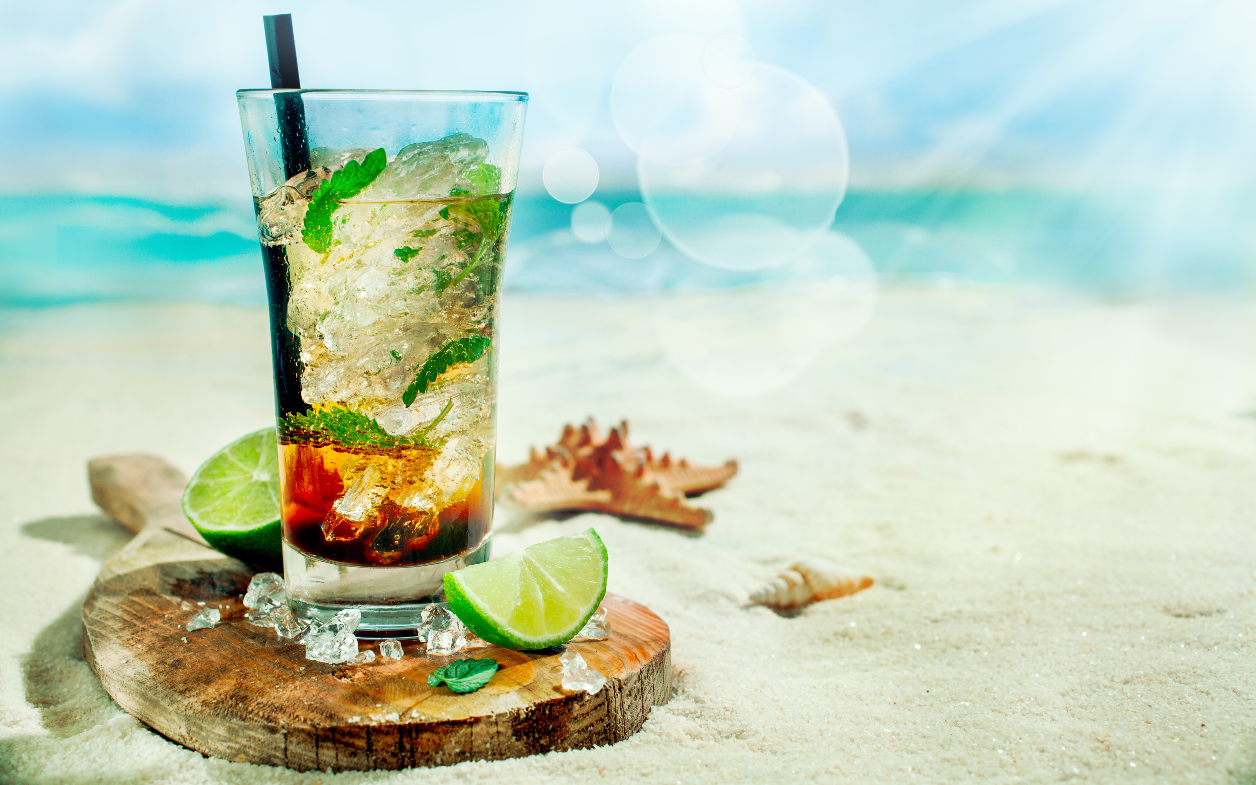 Коктейль в стакане с лаймом и кубиками льда стоит на песке на пляже