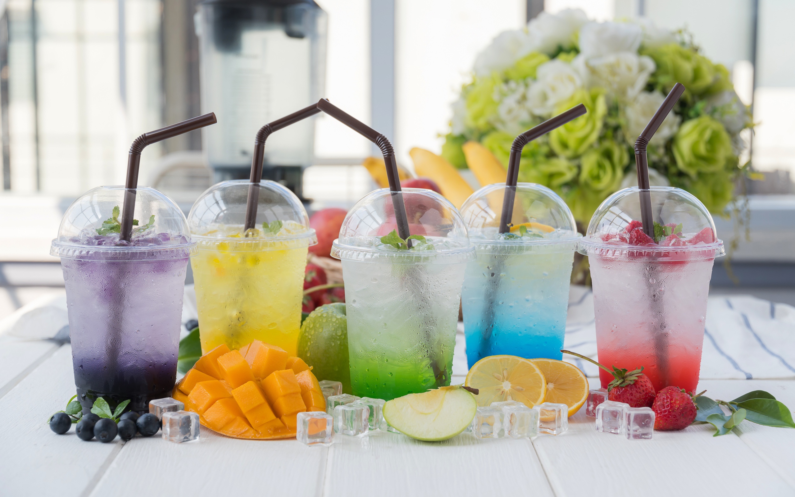 Коктейли в стаканах с трубочками на столе с кубиками льда и фруктами