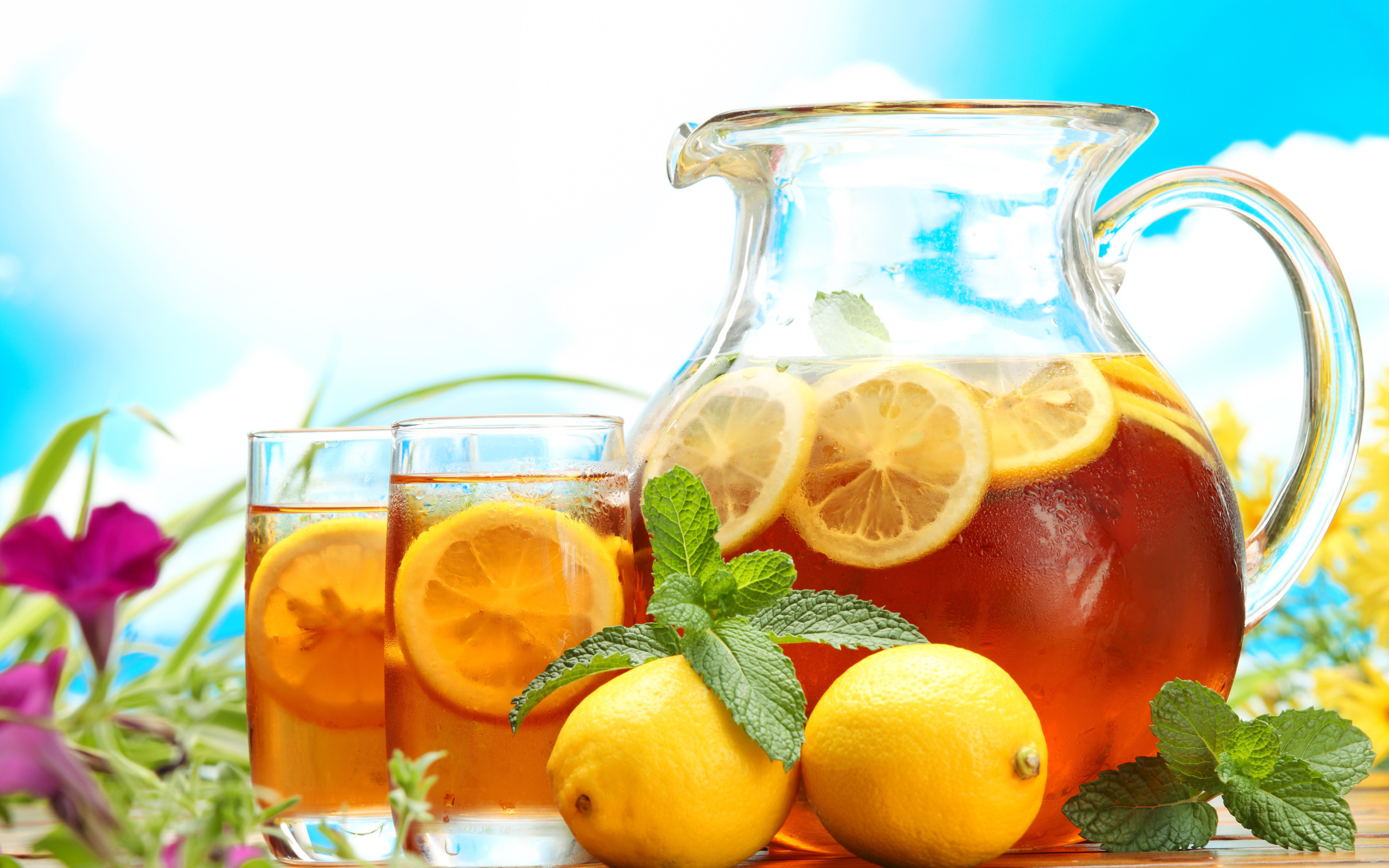 Холодный лимонад в графине на столе со стаканами и плодами лимона