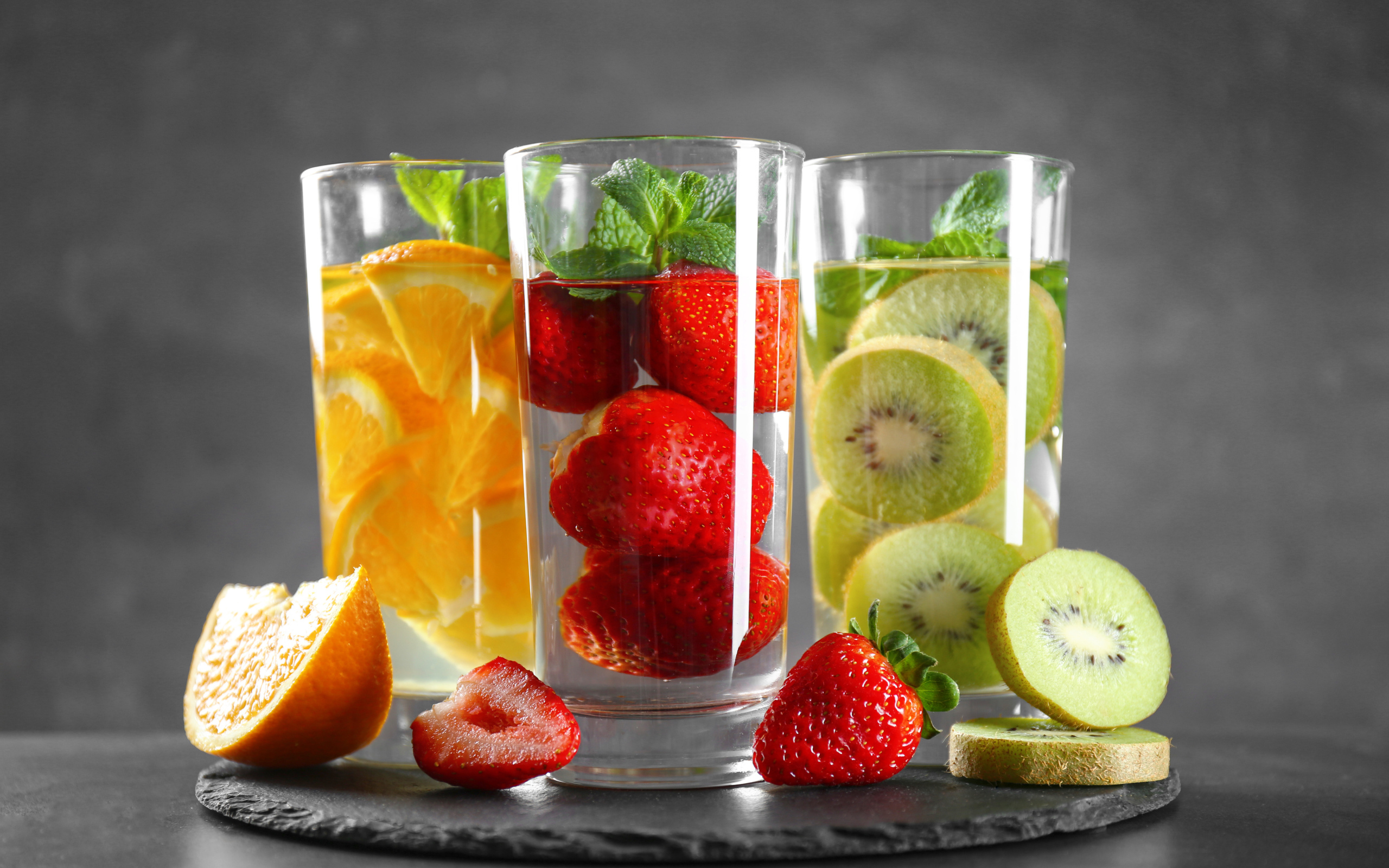 Напитки в стаканах с клубникой, киви и апельсинами на сером фоне