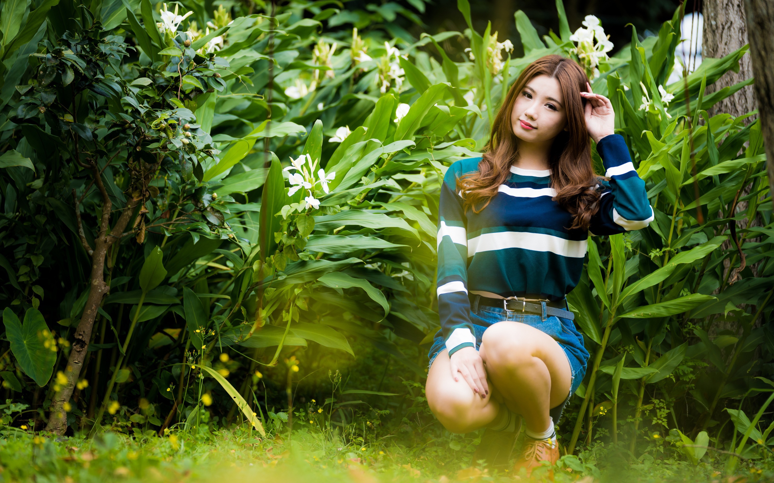 Молодая азиатка сидит в зеленых листьях 