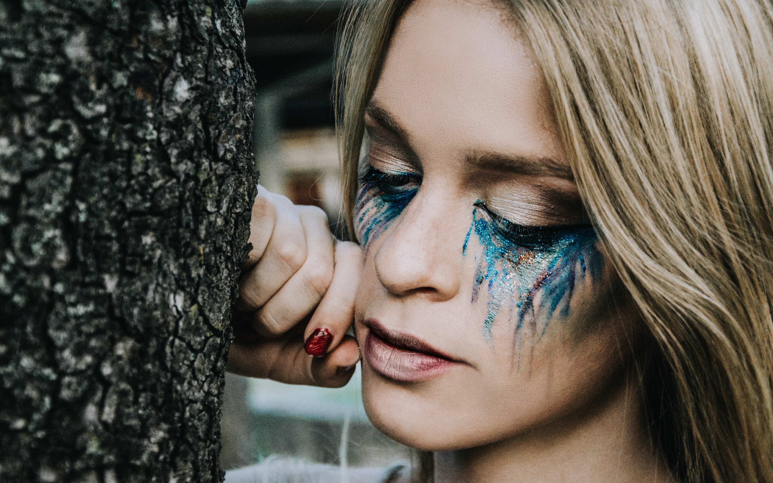 Заплаканная блондинка стоит у дерева