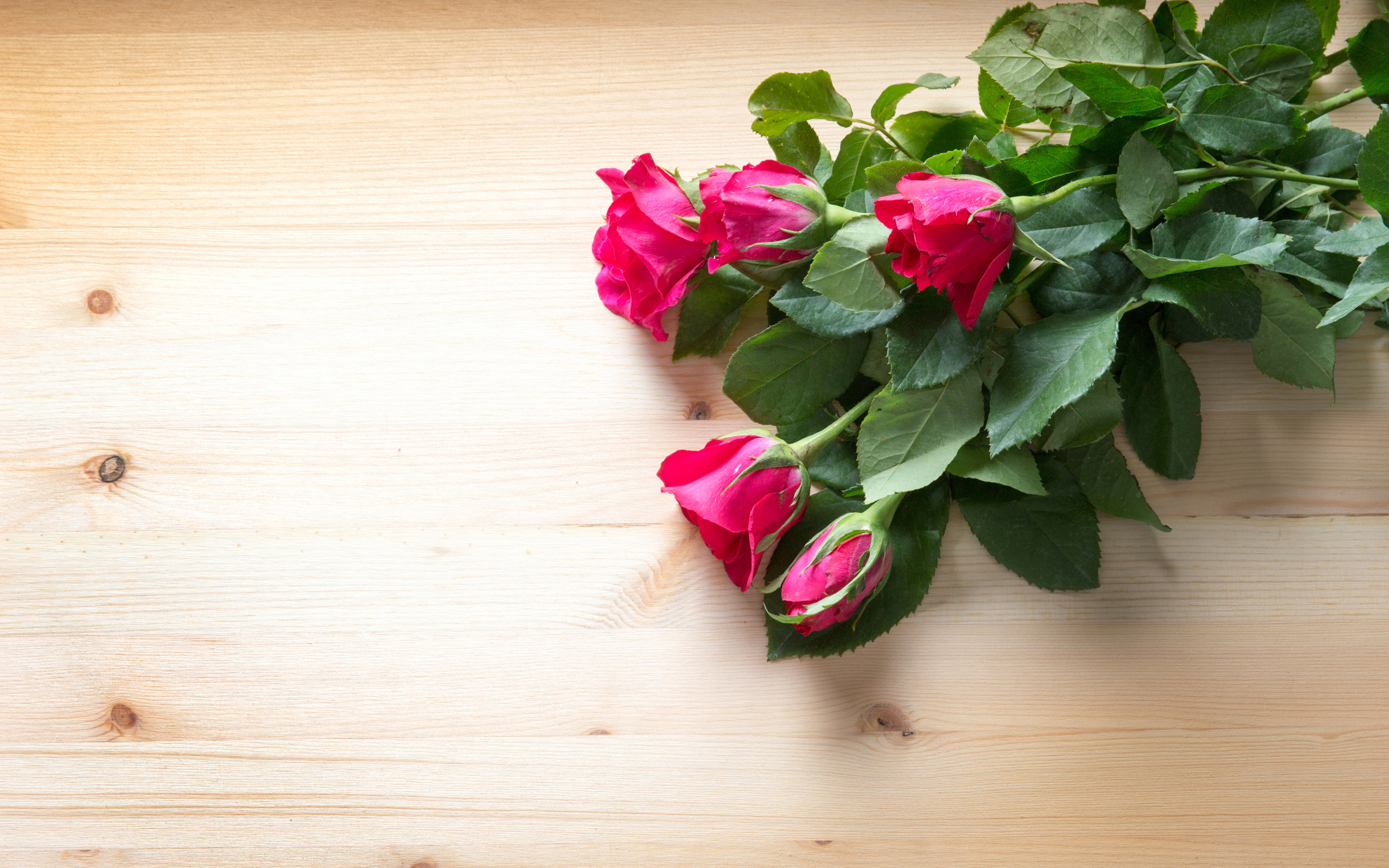 Букет розовых роз с зелеными листьями на деревянной поверхности 