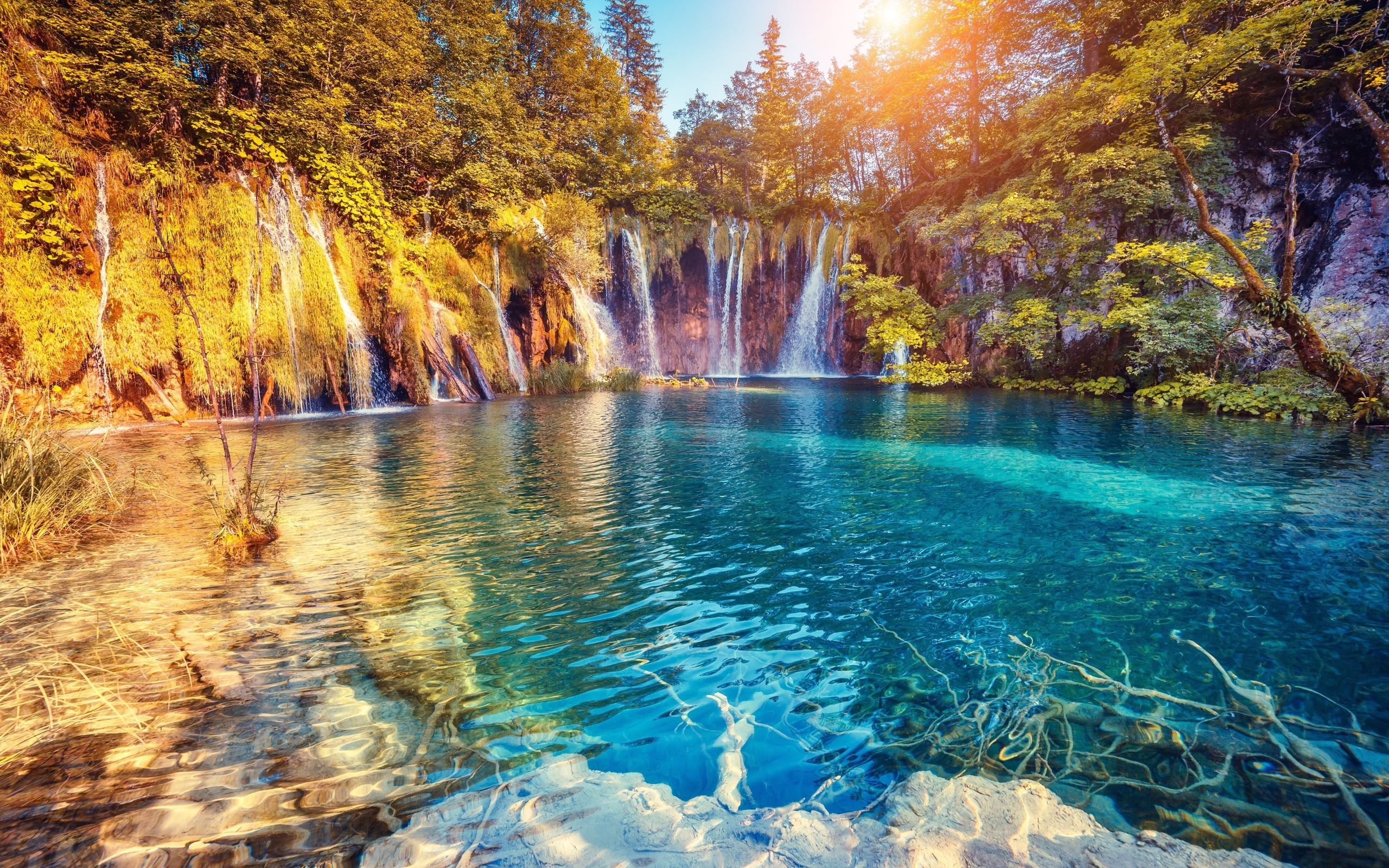 Водопад в лучах солнца стекает со скалы в реку