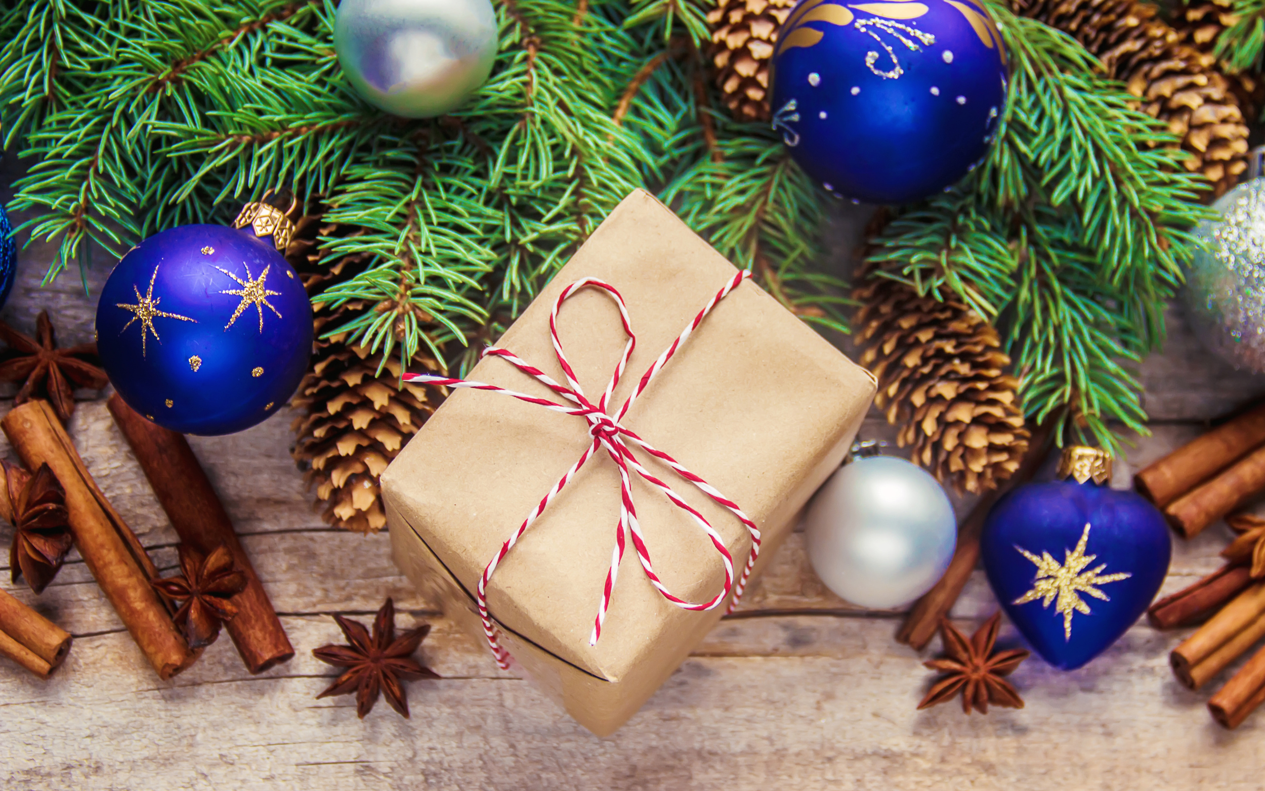 Еловая ветка с игрушками на столе с корицей и подарком на Новый год 