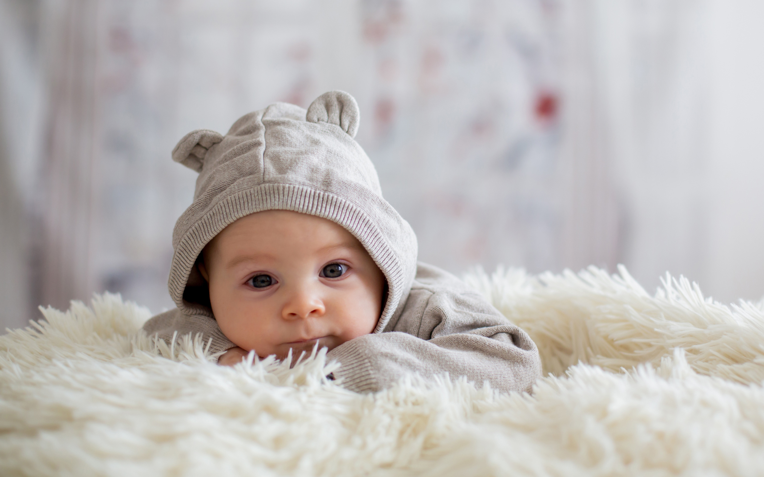 Маленький ребенок лежит на белом меховом покрывале 