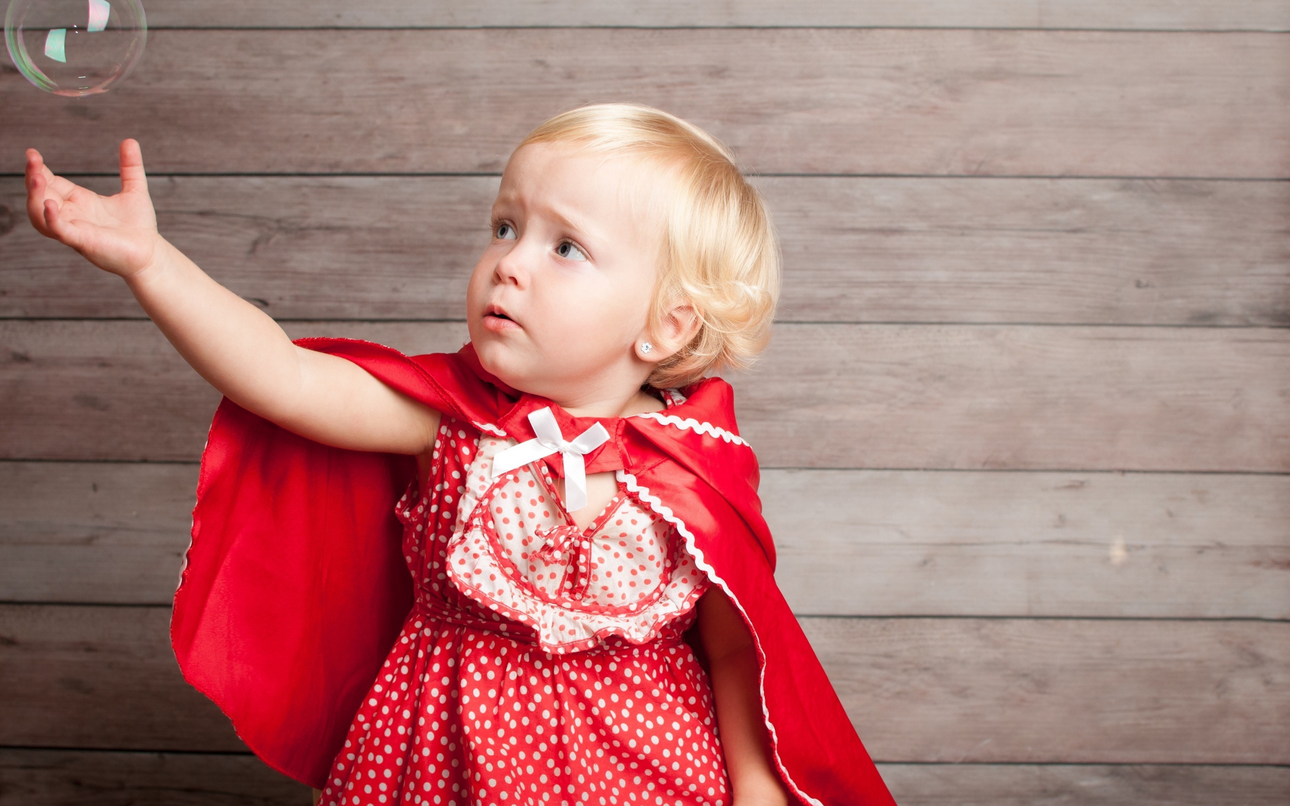Маленькая девочка в красном платье ловит мыльный пузырь