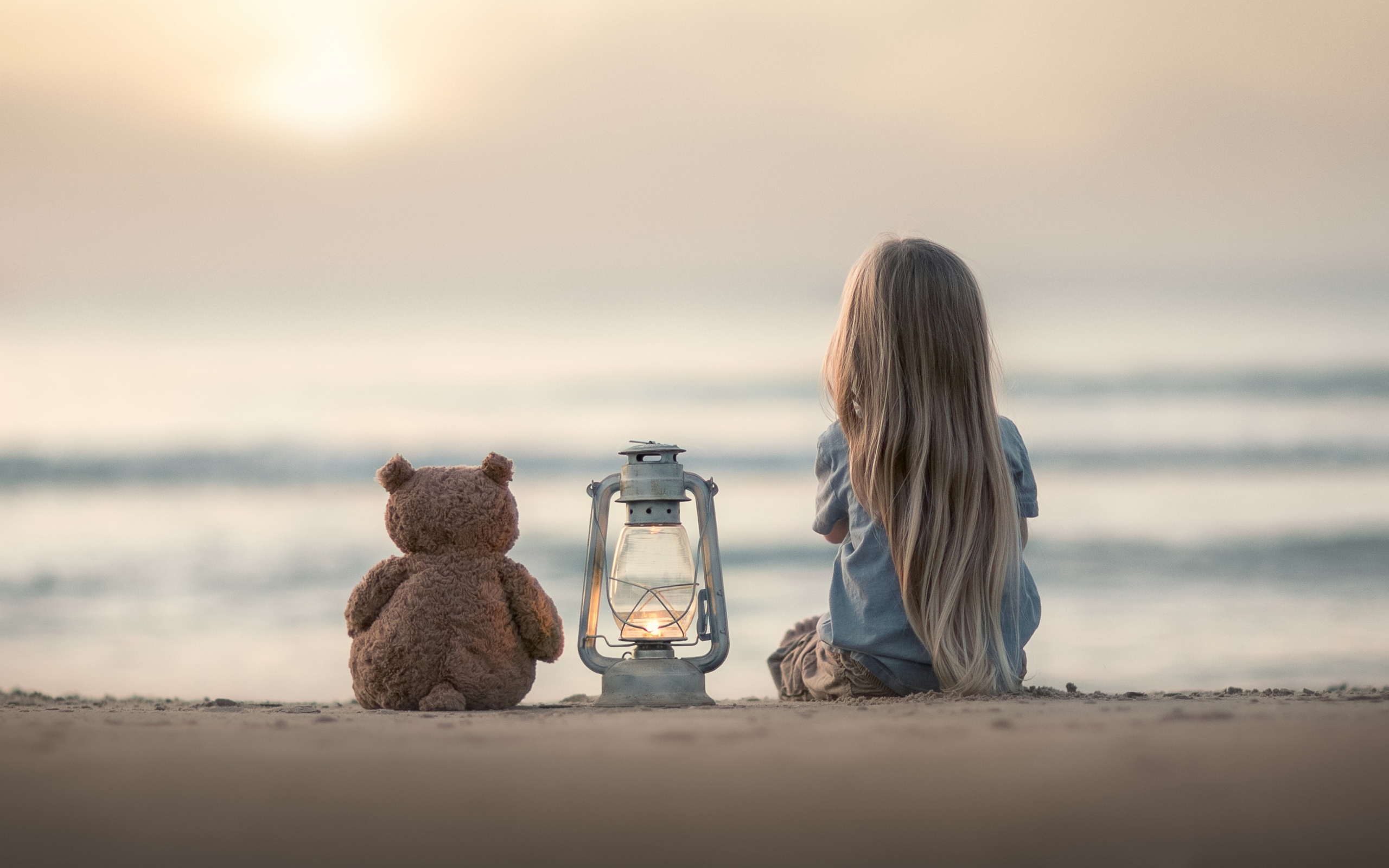 Маленькая девочка сидит на песке с плюшевым мишкой 