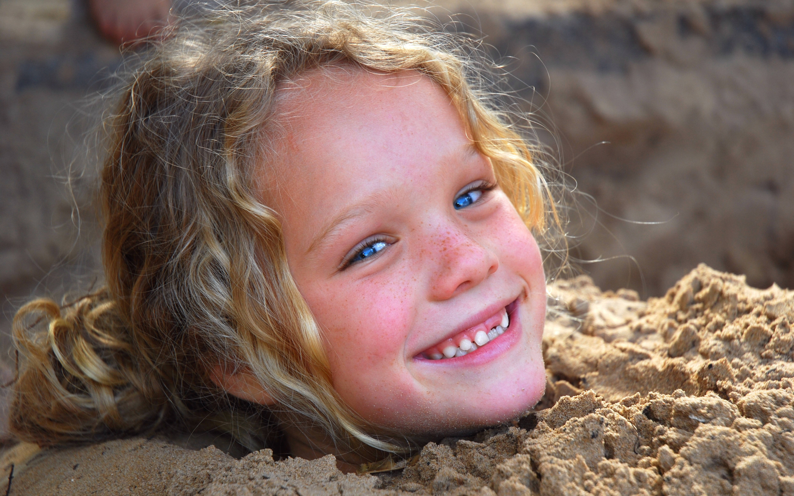 Маленькая улыбающаяся девочка играет в песке