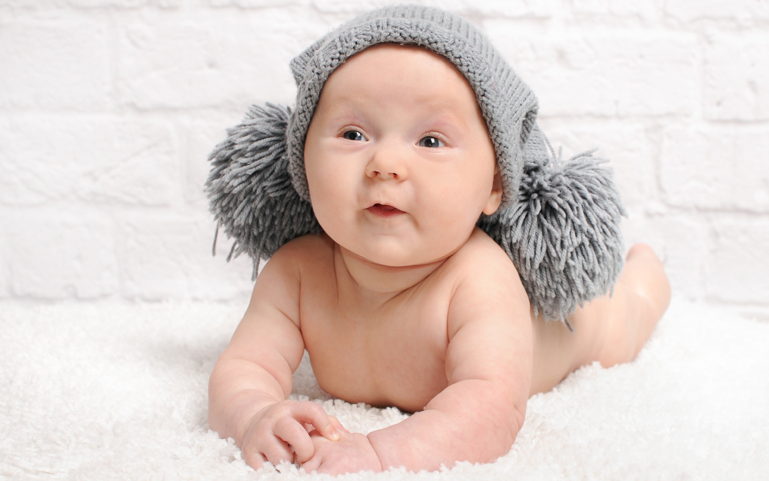 Улыбающийся грудной ребенок в серой шапке с бубонами