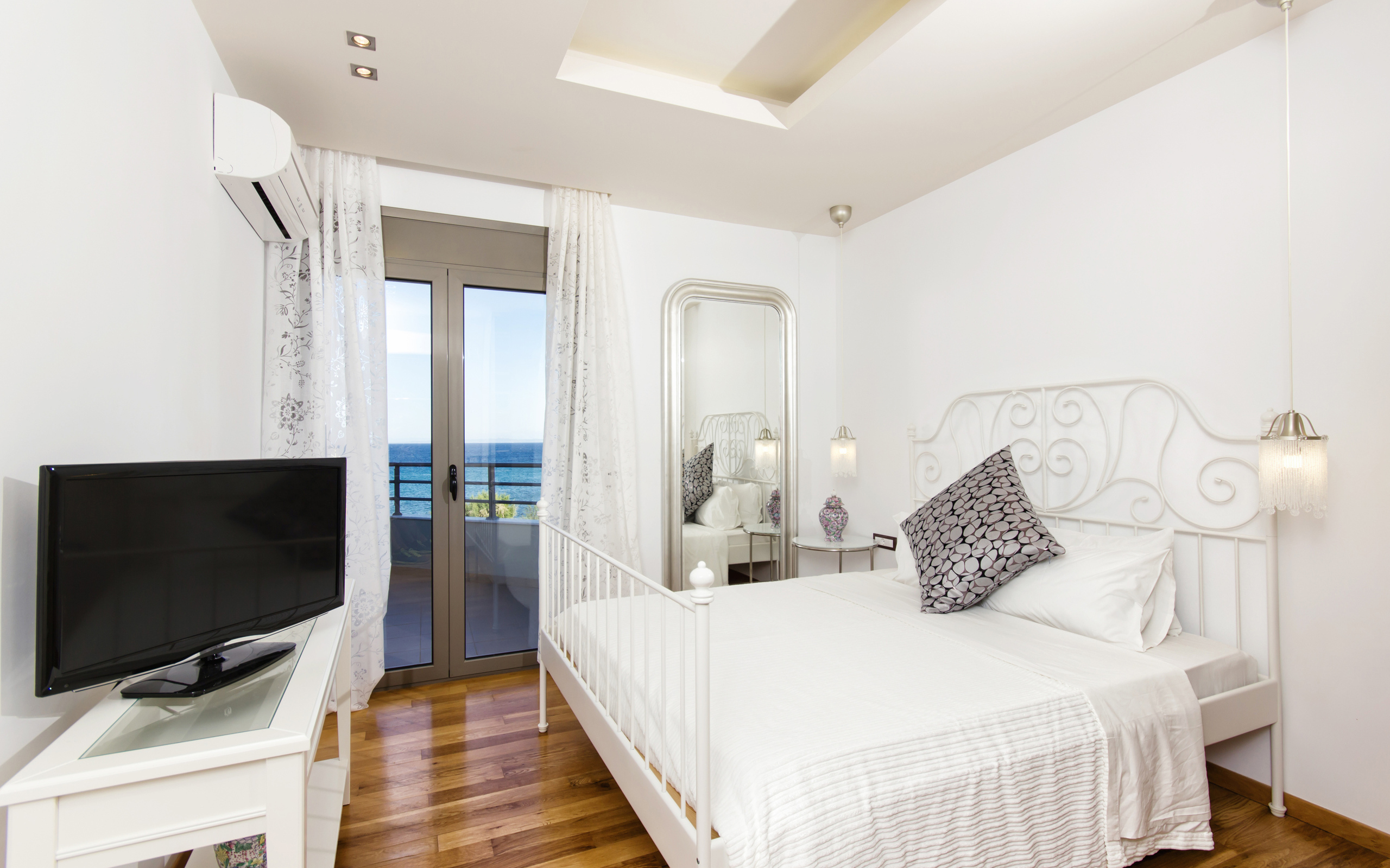 Светлая спальня с большой белой кроватью и телевизором 