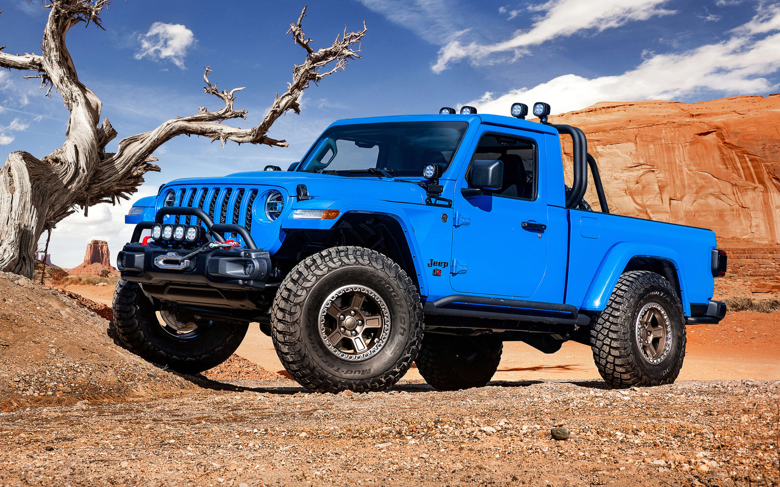 Синий пикап Jeep J6, 2019 года на фоне гор у сухого дерева
