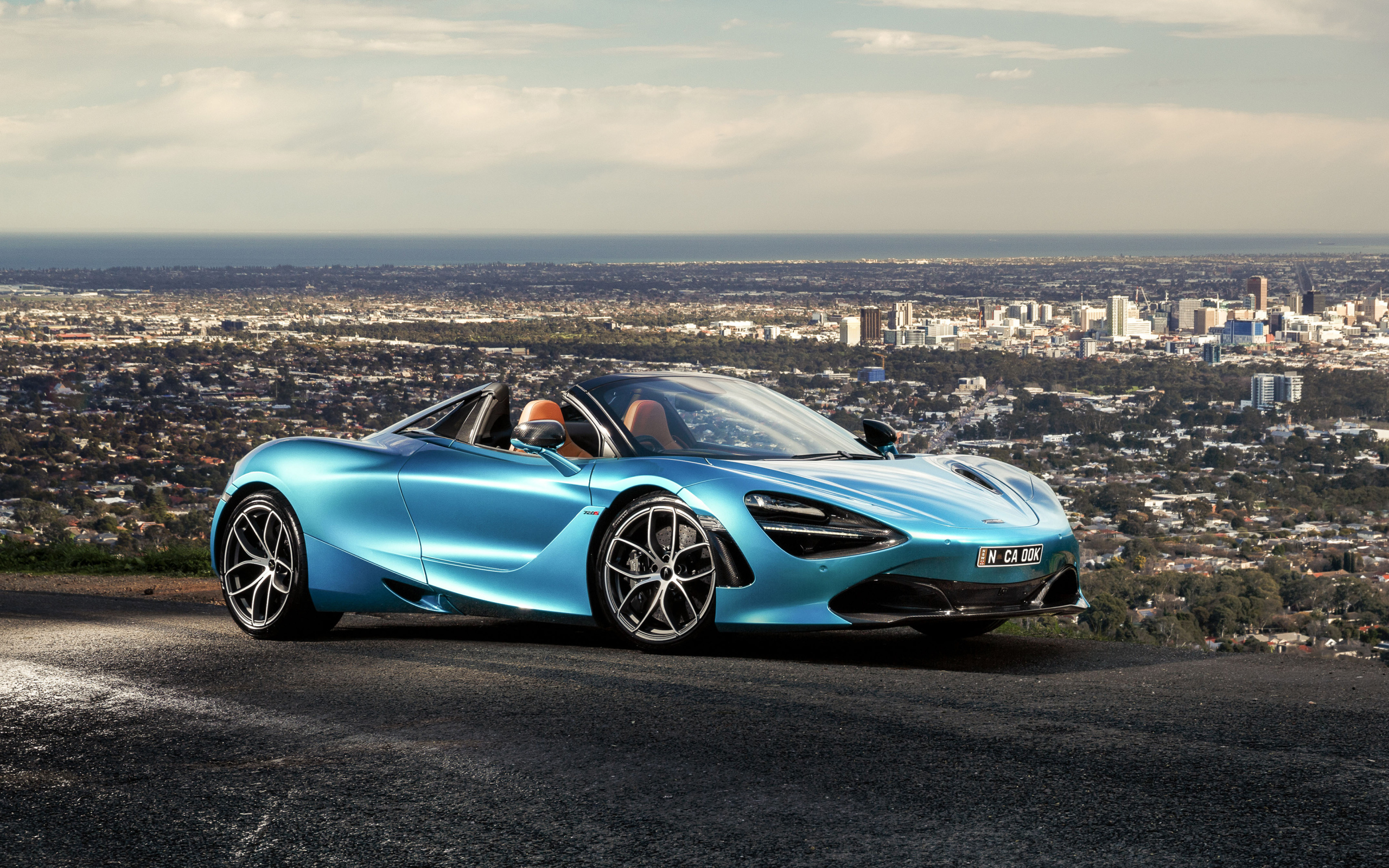 Голубой спортивный автомобиль McLaren 720S Spider 2019 года на фоне города