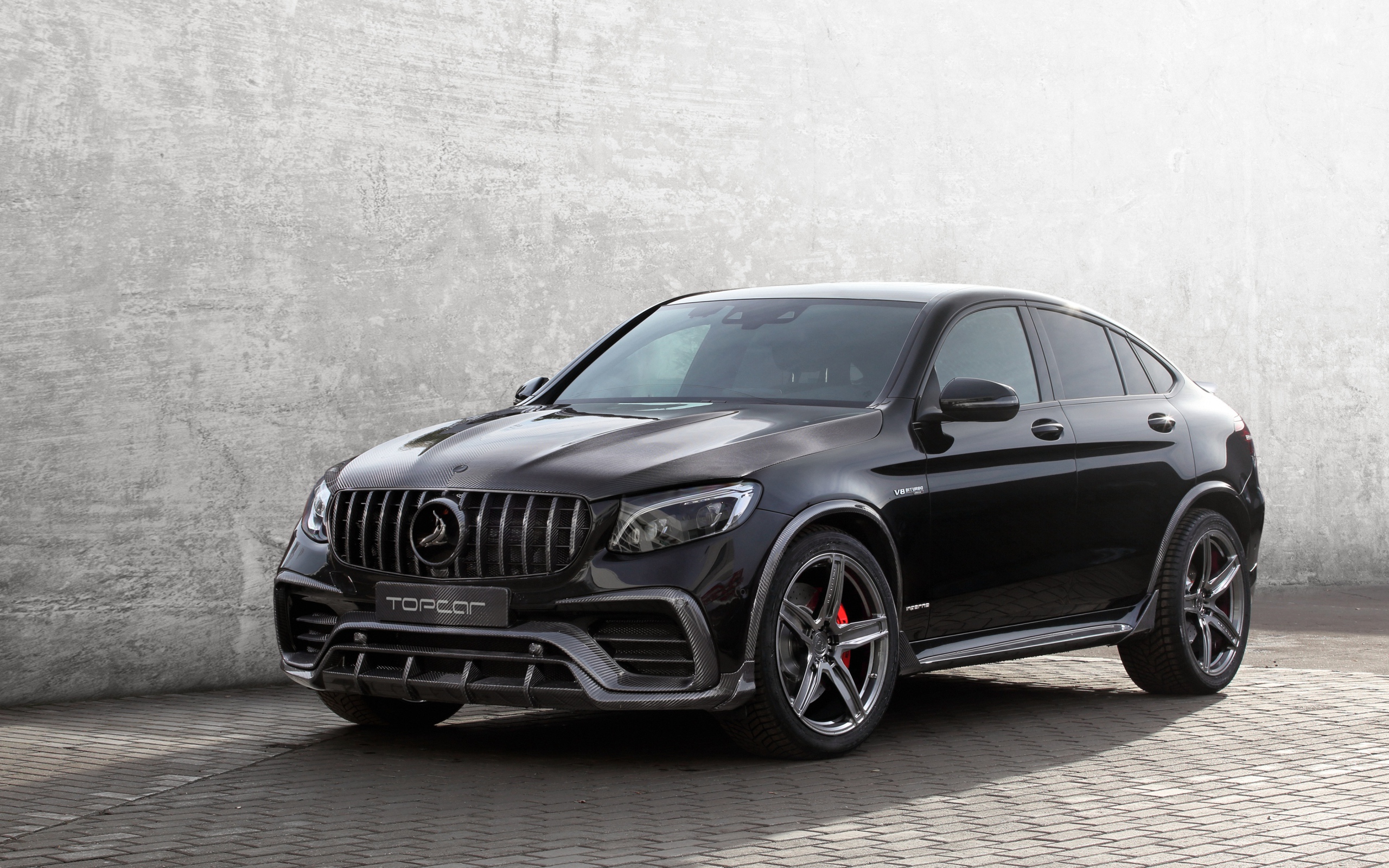 Черный автомобиль Mercedes-AMG GLC 63 на фоне серой стены 