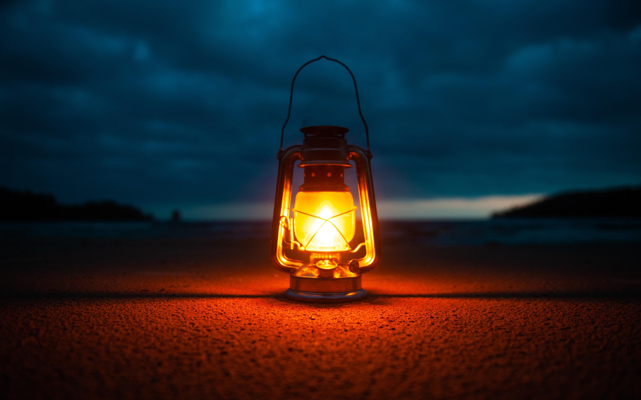 Включенный фонарь стоит на песке у моря 