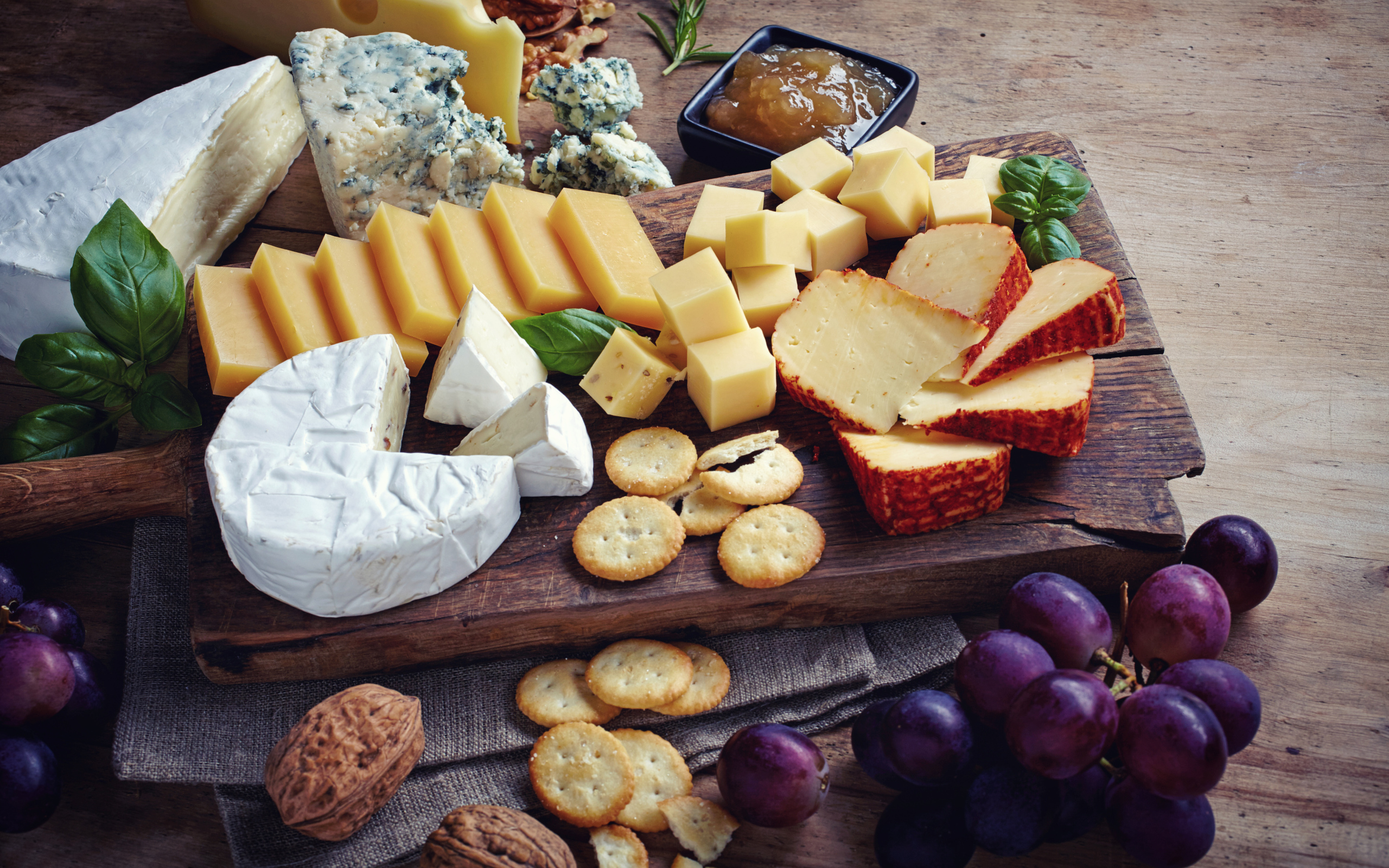 Сырная нарезка на разделочной доске на столе с виноградом и крекерами