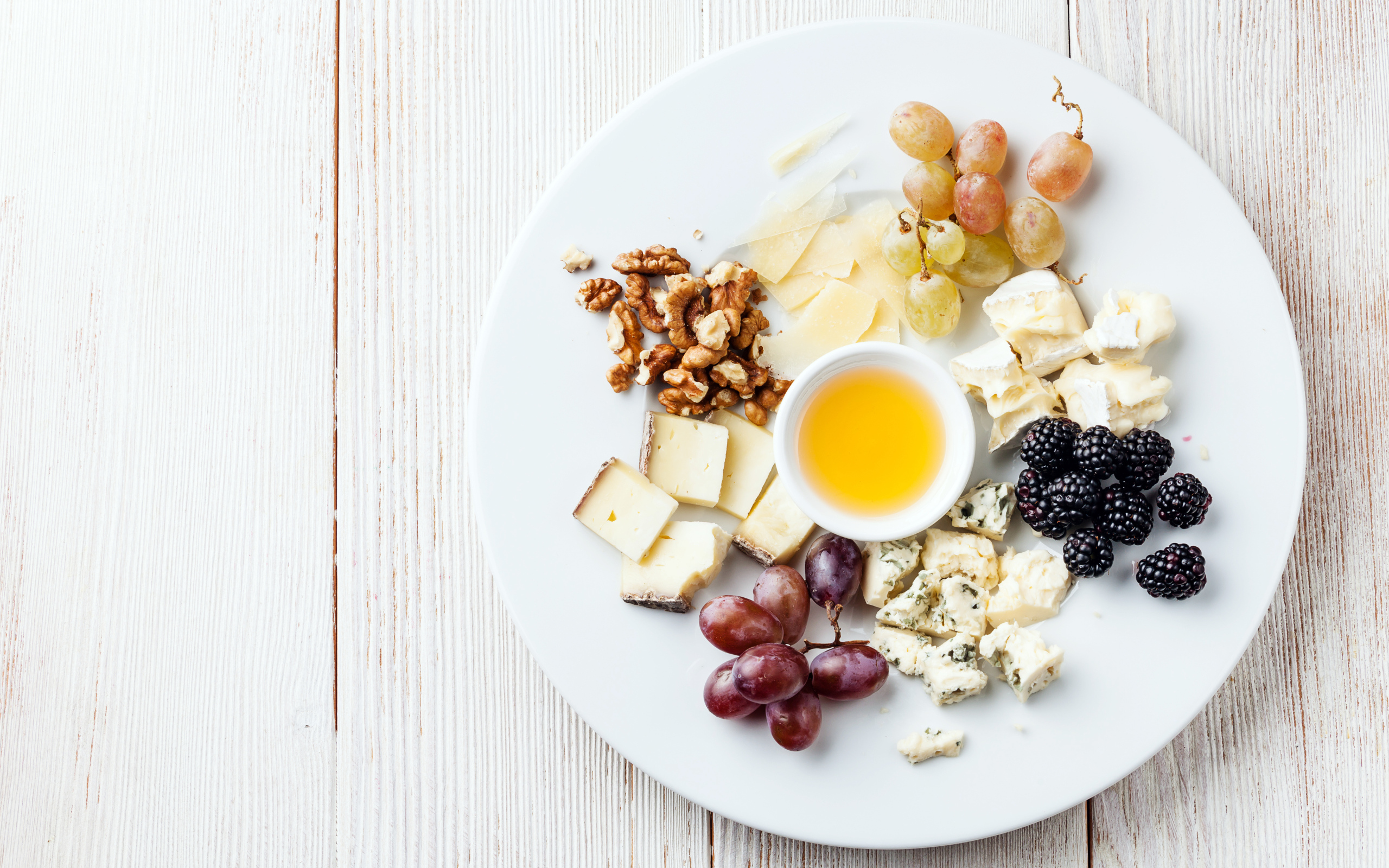 Куски сыра на тарелке с орехами, виноградом, медом и ягодами ежевики