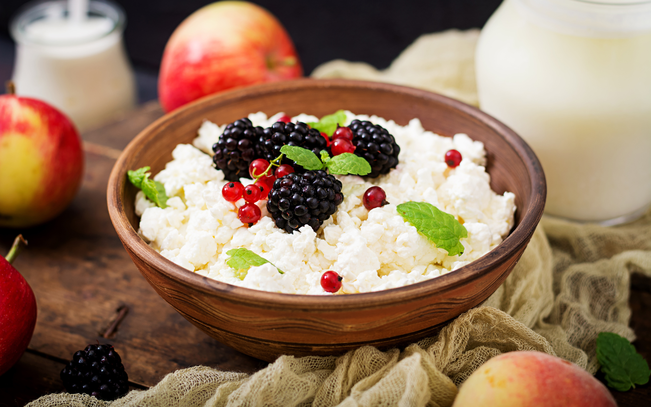 Творог с ягодами в деревянной миске на столе с яблоками
