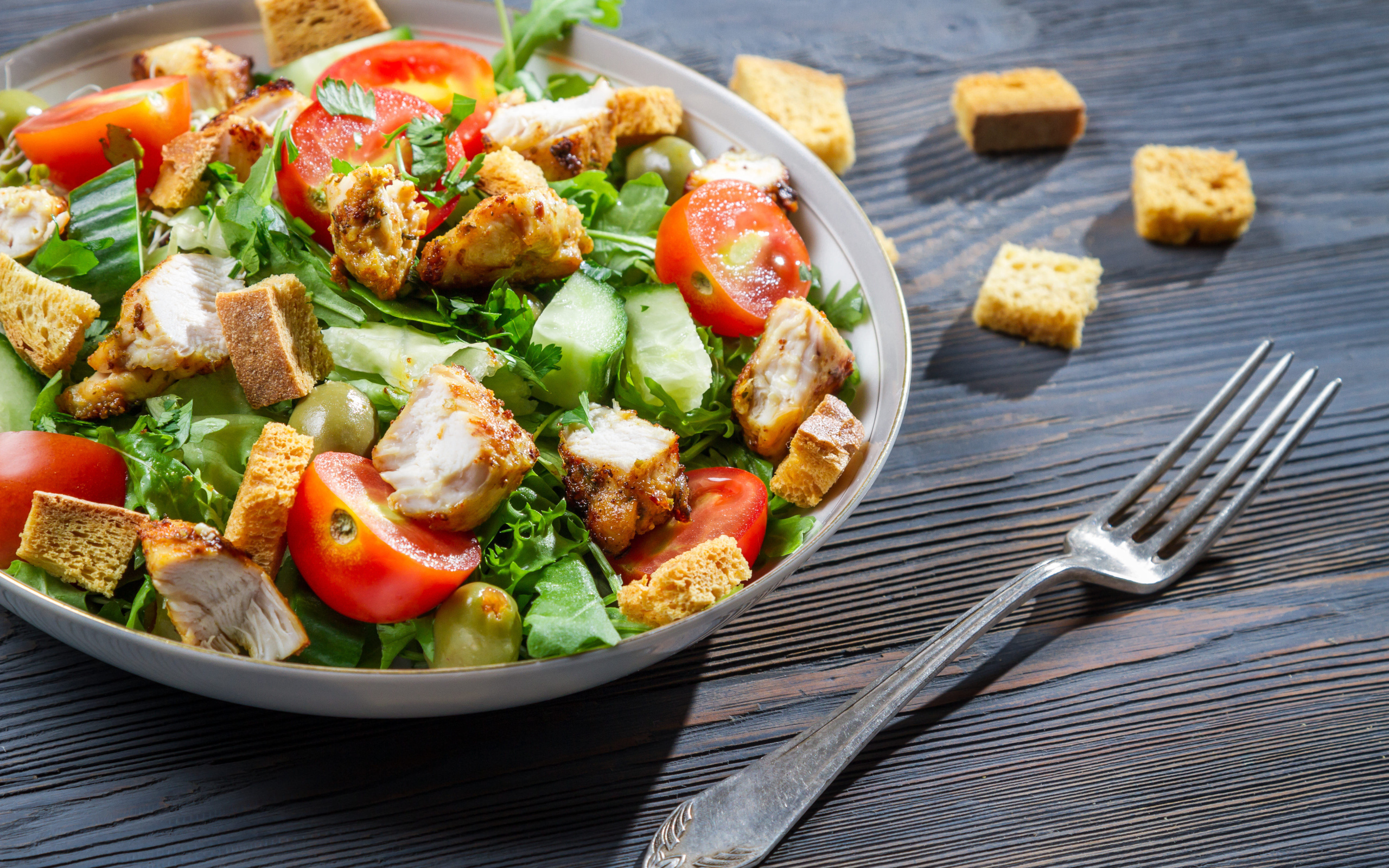 Салат с овощами, сухариками и курицей и на столе с вилкой