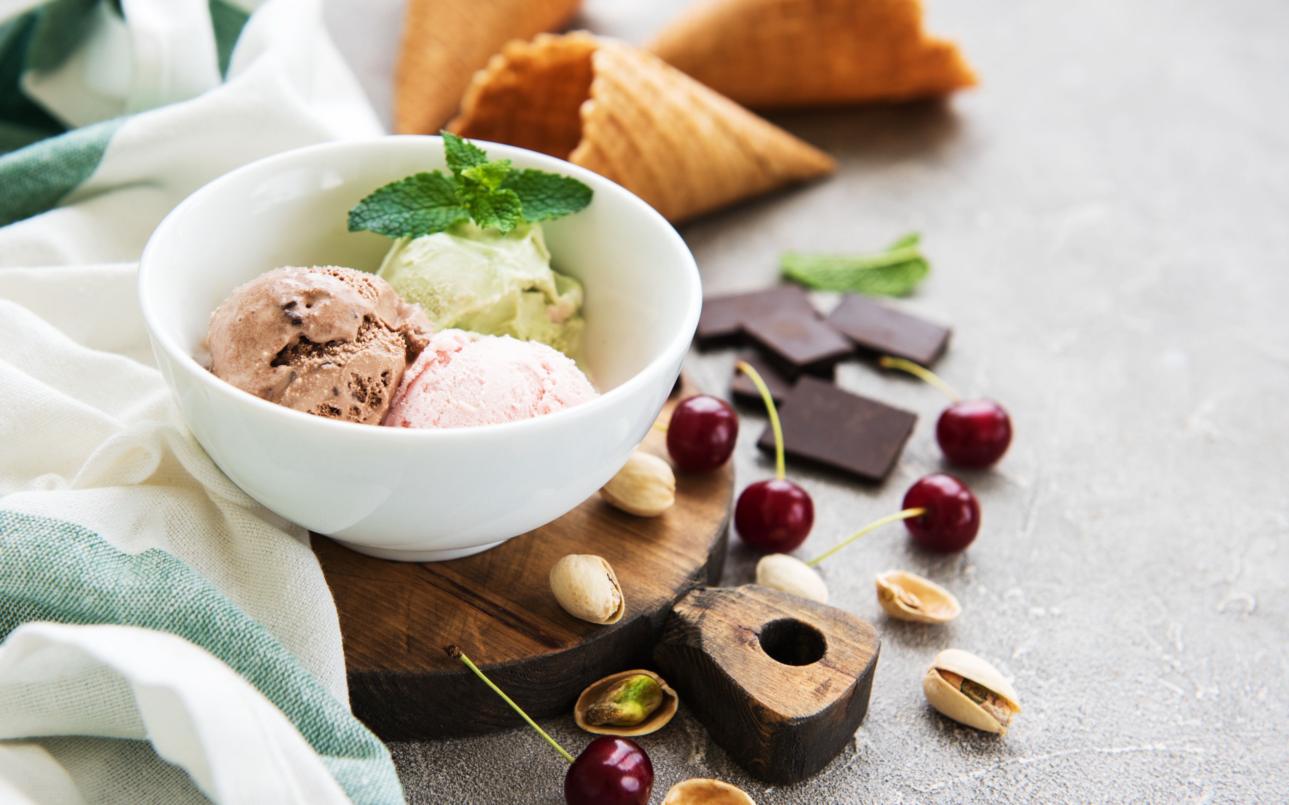 Шарики мороженого на столе вафельными рожками, черешней и фисташками