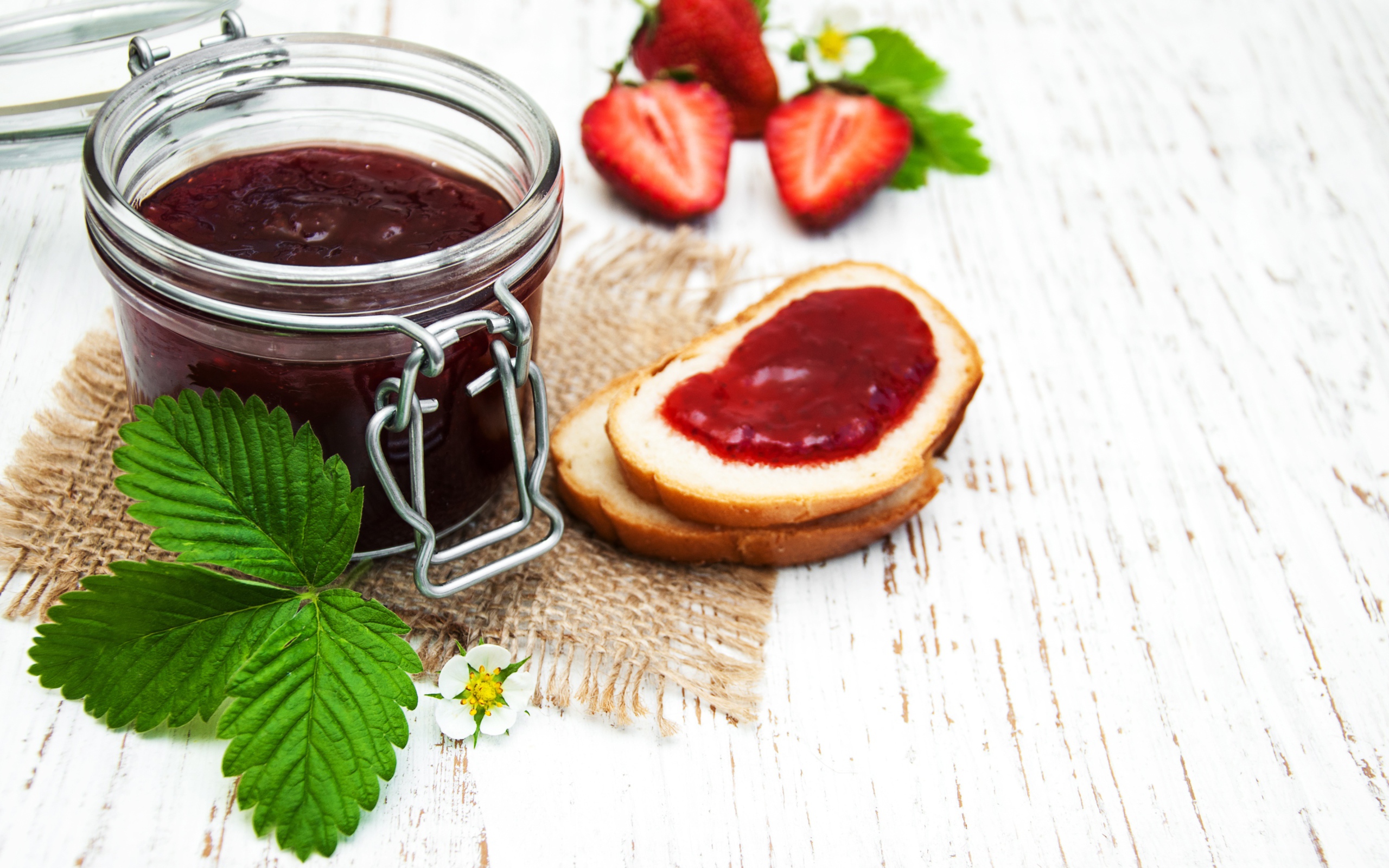 Банка клубничного джема на столе с батоном