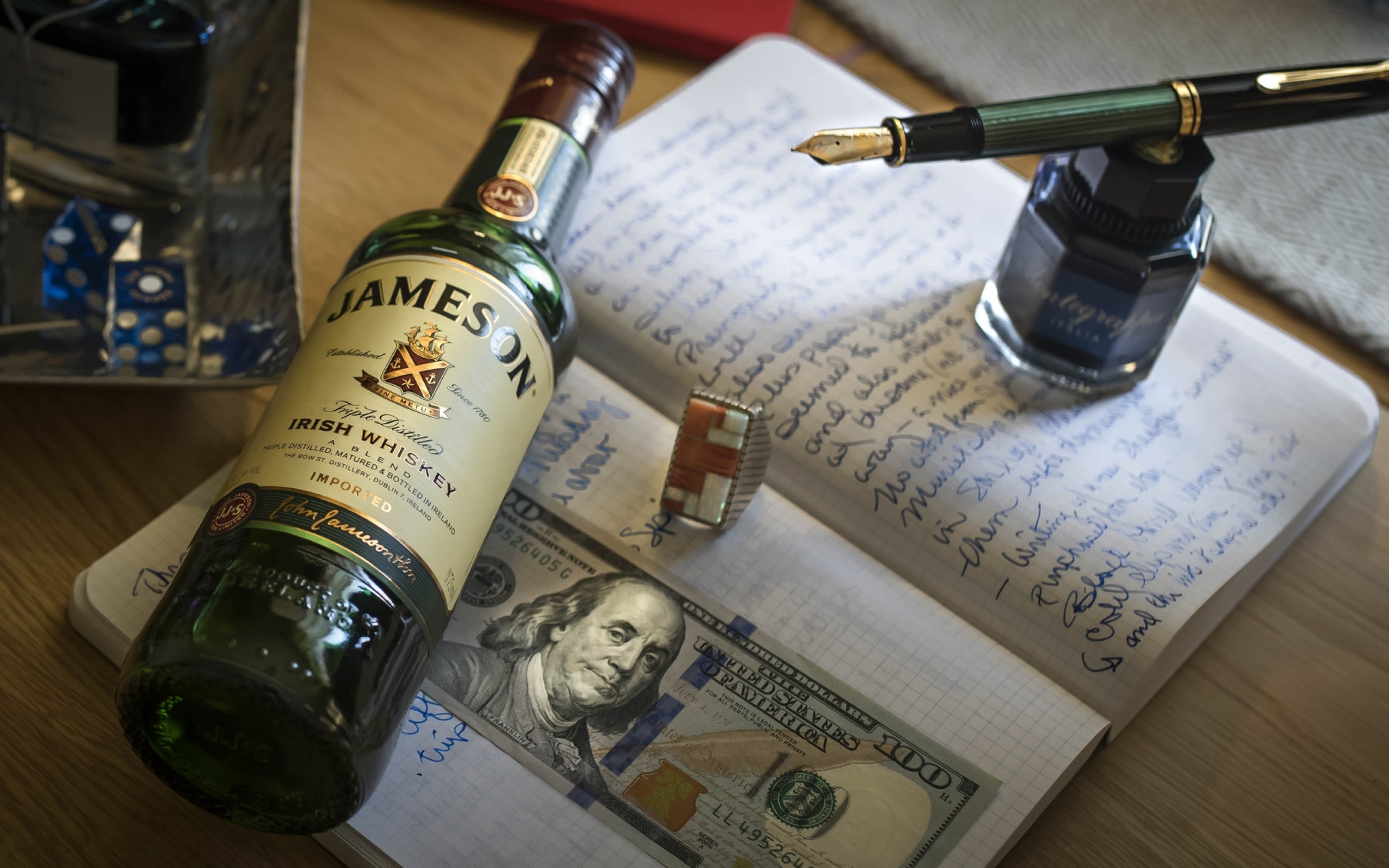 Бутылка виски лежит на тетради с чернильницей и купюрой