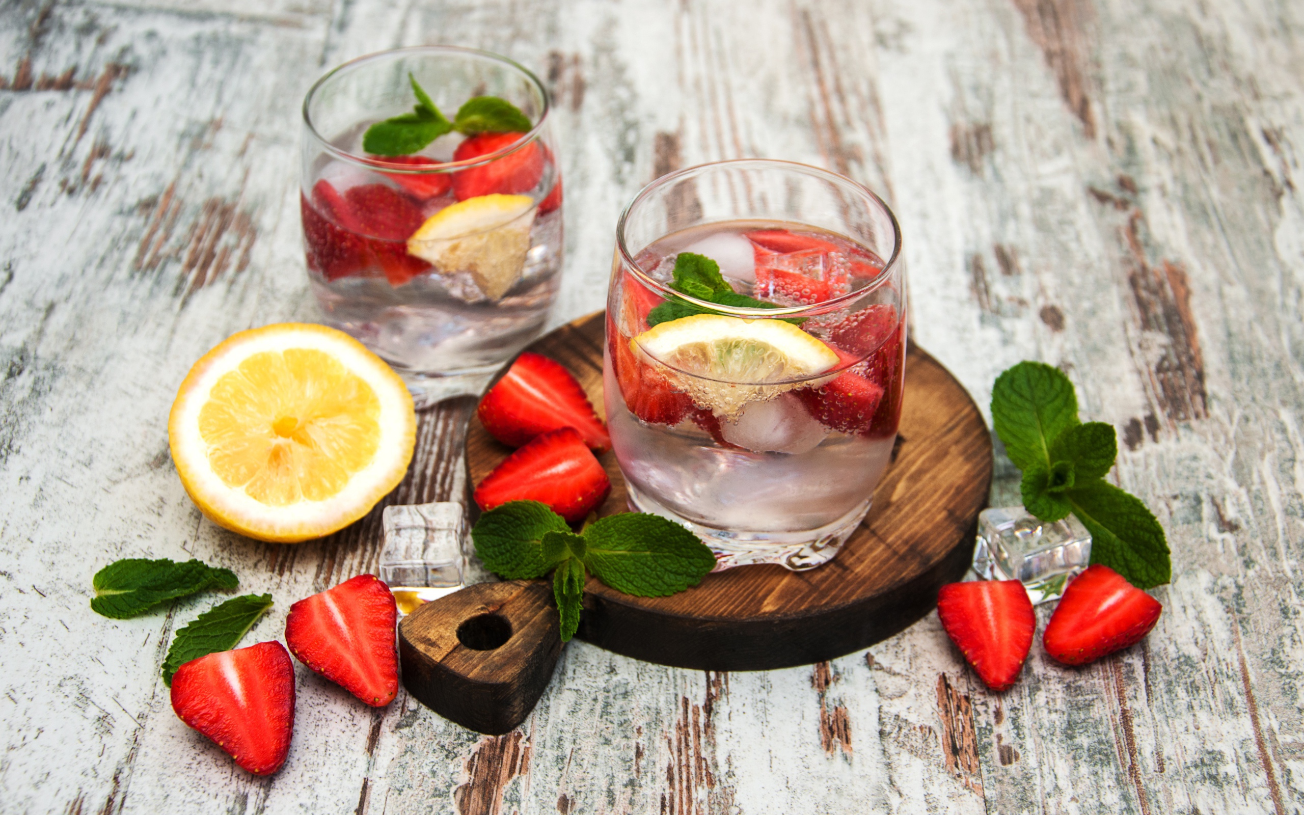 Холодный мохито на столе с ягодами клубники, лимоном и мятой