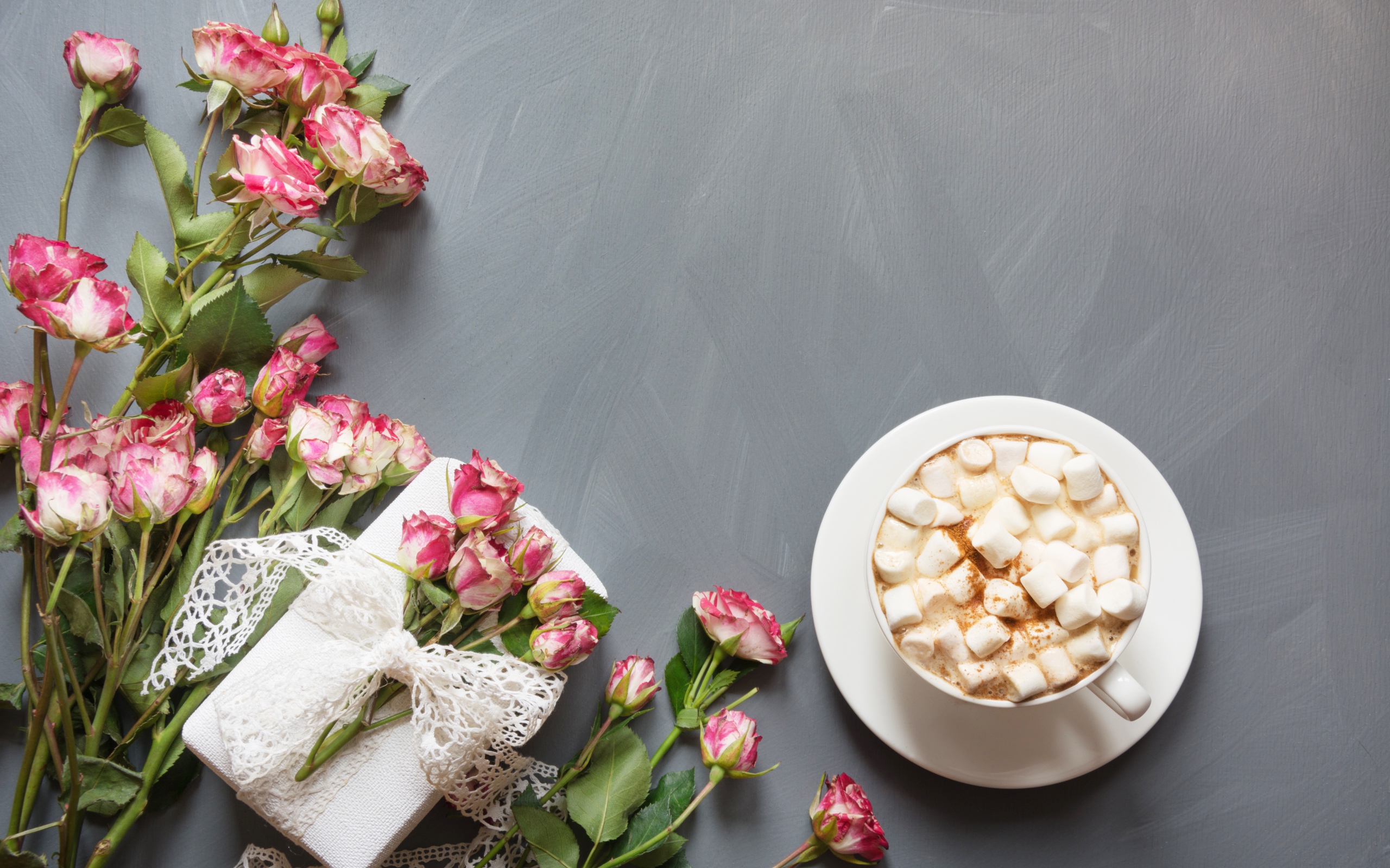 Чашка кофе с маршмеллоу на столе с подарком и букетом роз