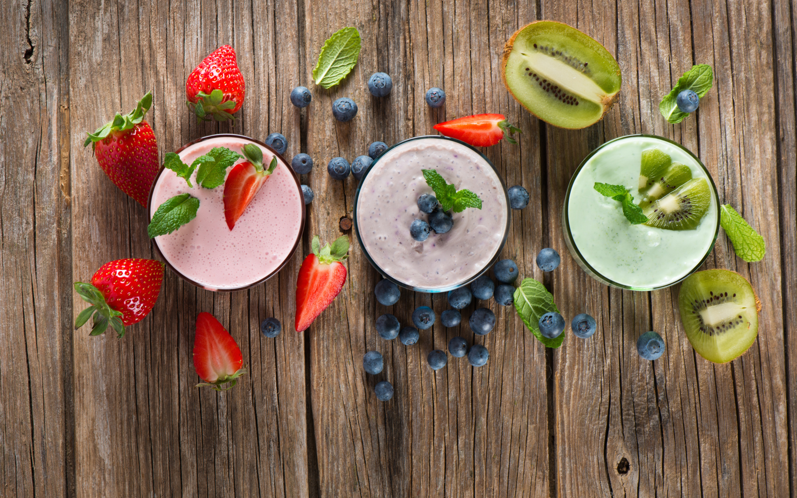 Стаканы со смузи на столе с киви, ягодами клубники и черники