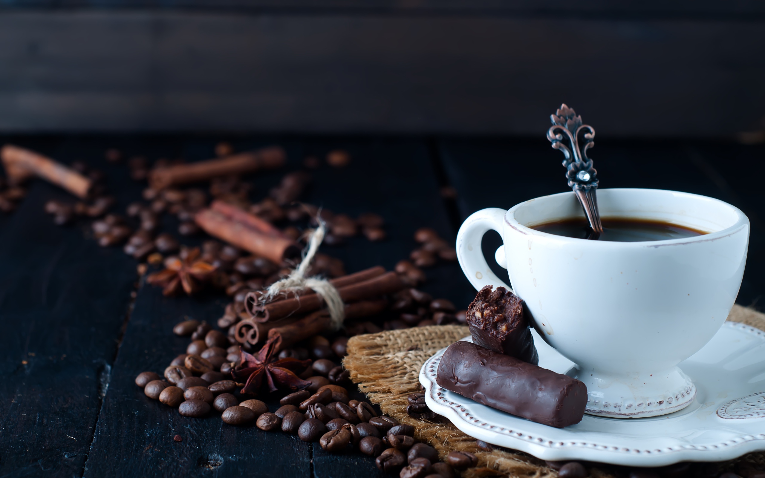 Белая чашка кофе на столе с конфетами, корицей, бадьяном и зернами