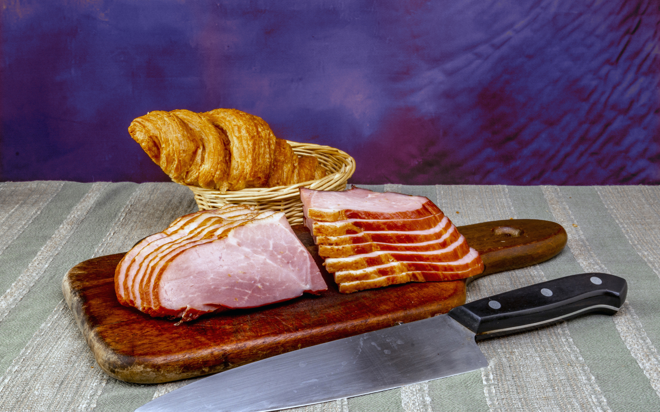 Кусок нарезанной ветчины на доске с круассаном