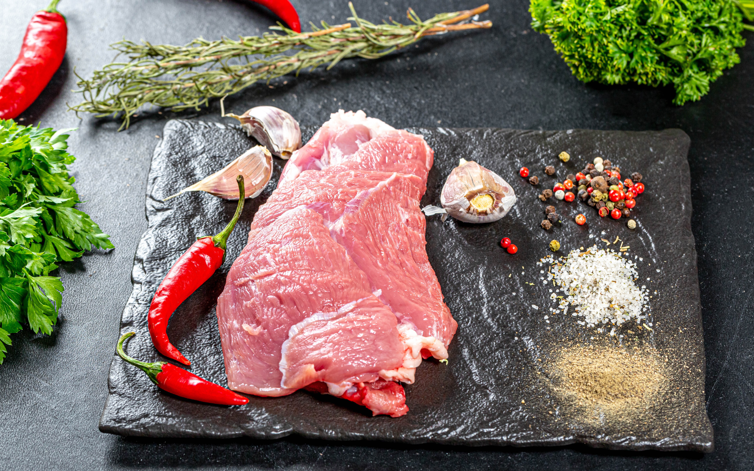 Кусок мяса на столе с острым перцем, чесноком и зеленью
