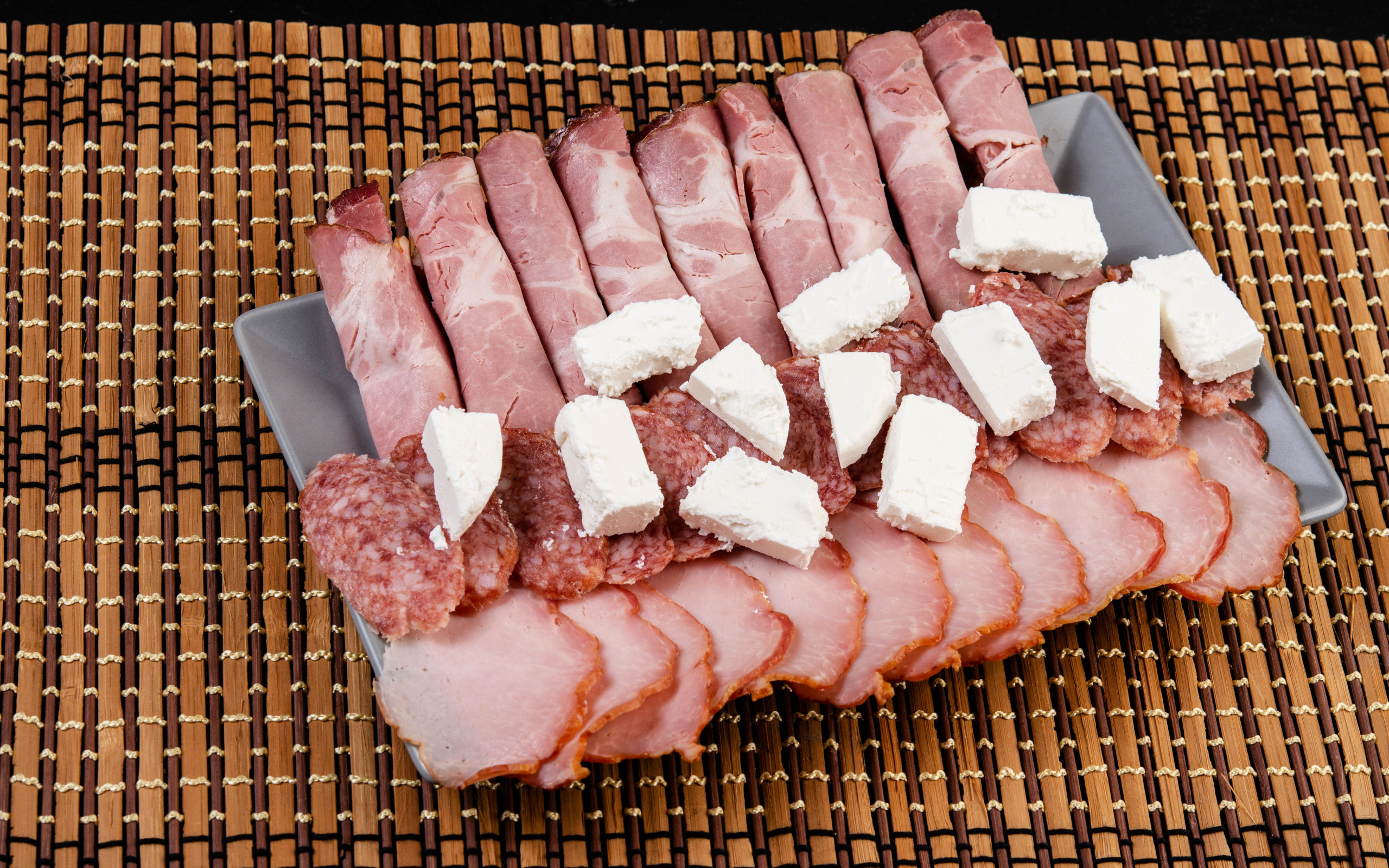 Колбаса и ветчина на тарелке с кусочками сыра фета