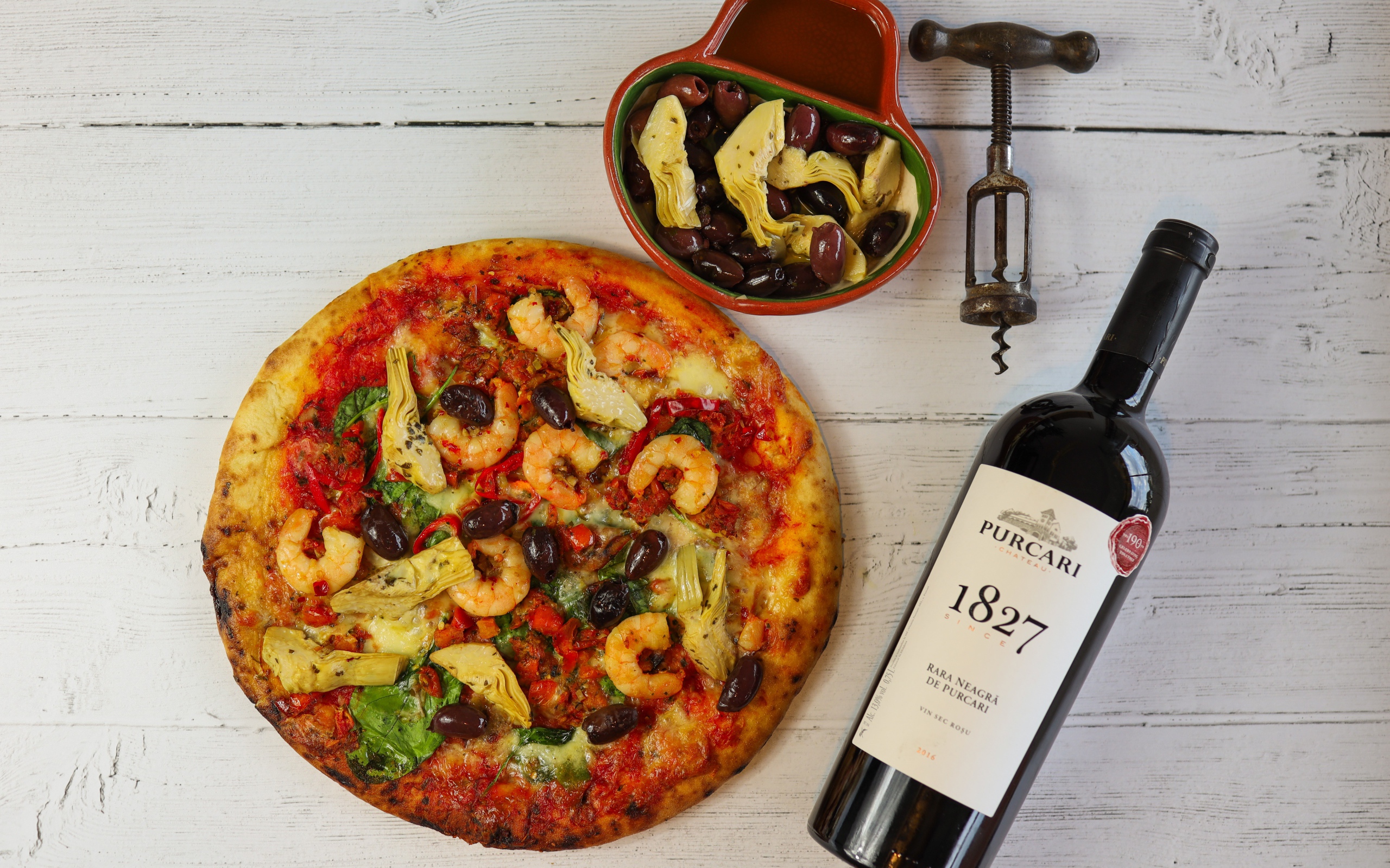 Пицца на столе с оливками и бутылкой вина