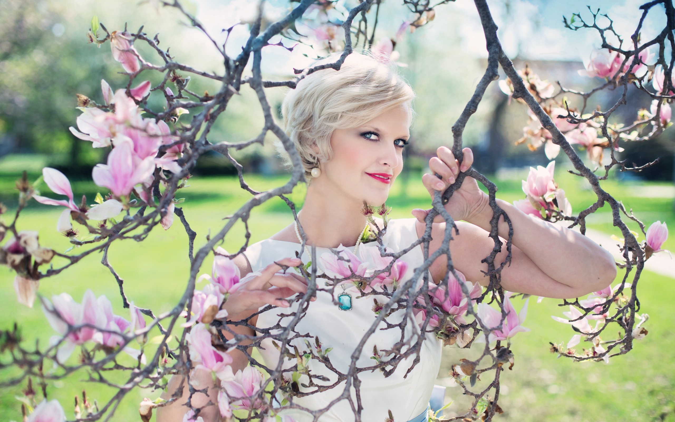 Красивая женщина с короткой стрижкой стоит у цветущей магнолии 