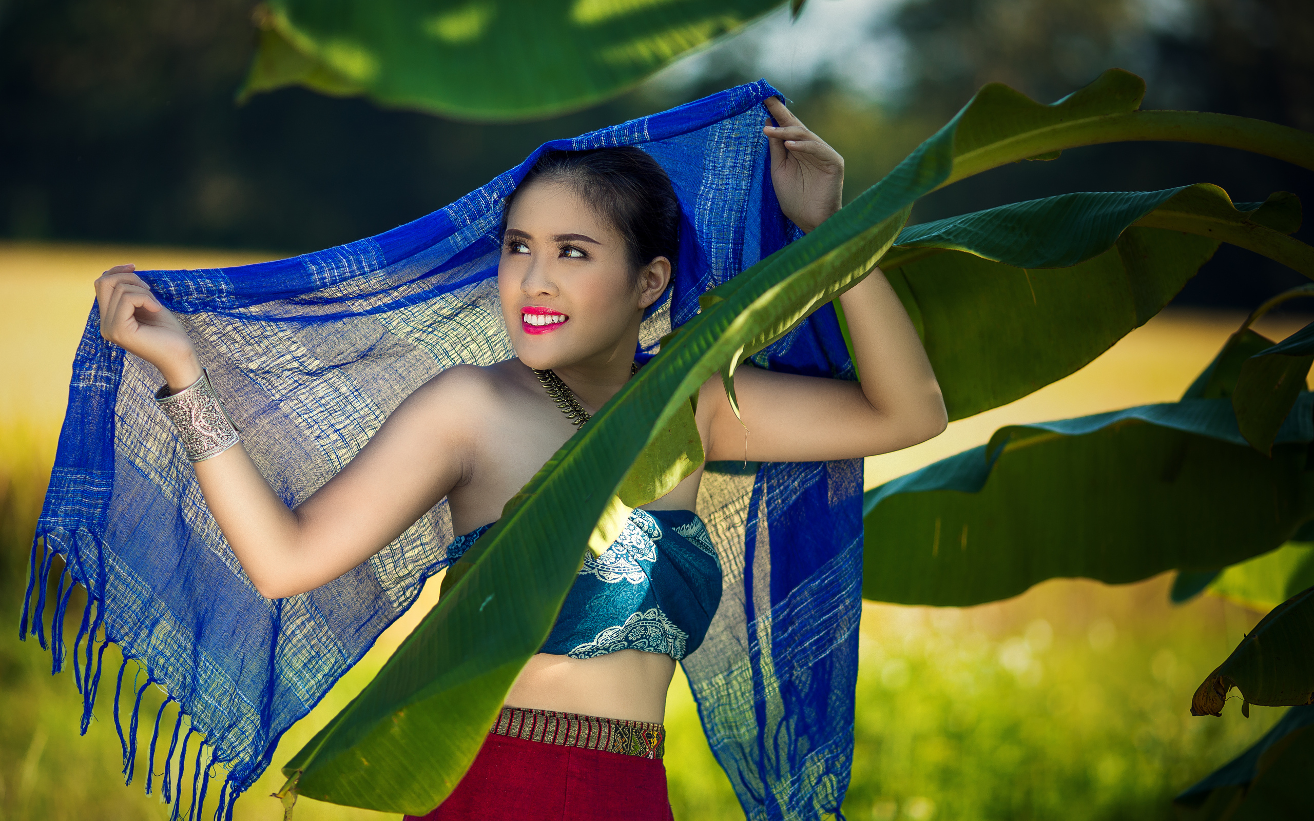 Красивая девушка азиатка с синим палантином у зеленых листьев