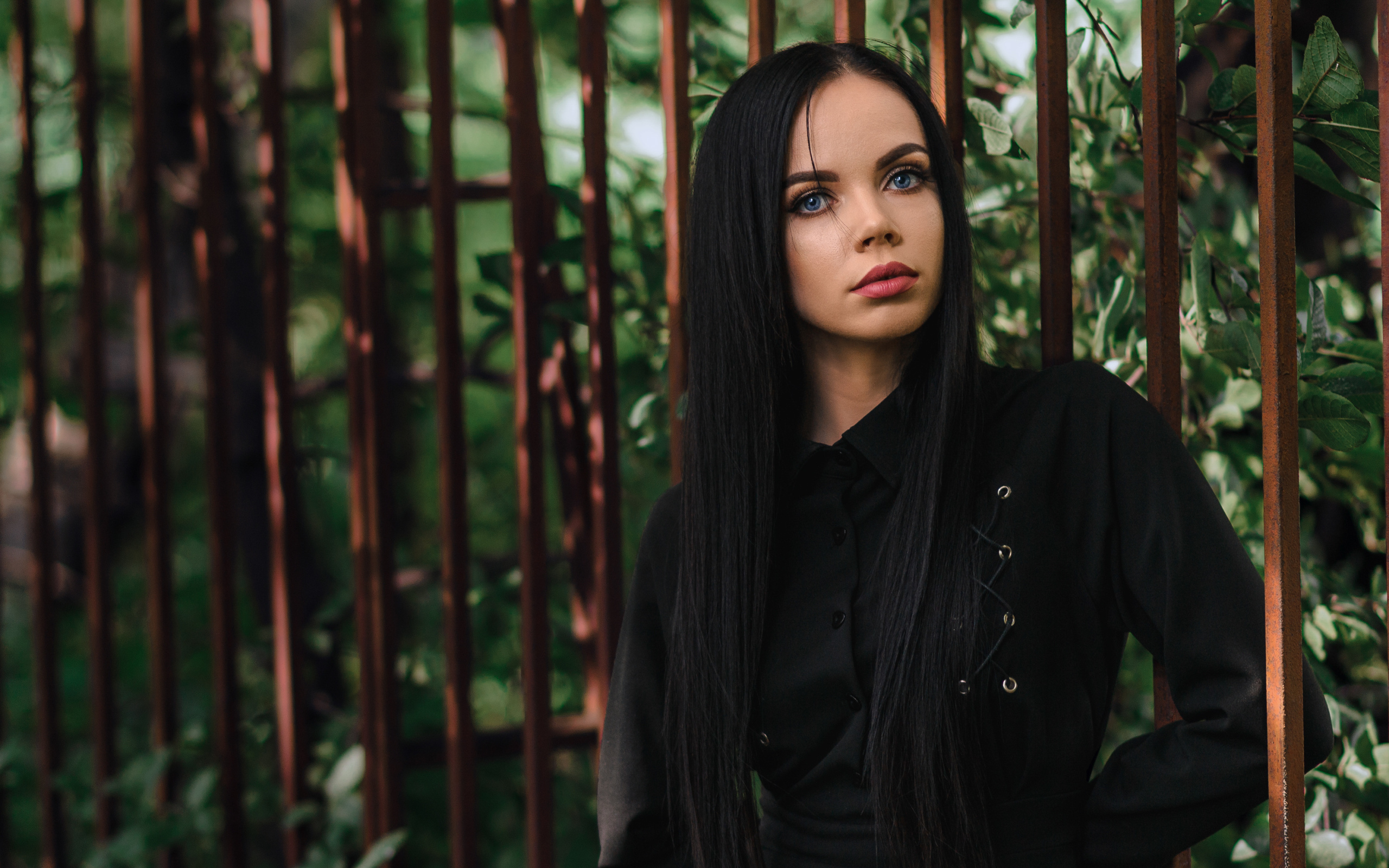 Красивая голубоглазая девушка в черном платье у железного забора
