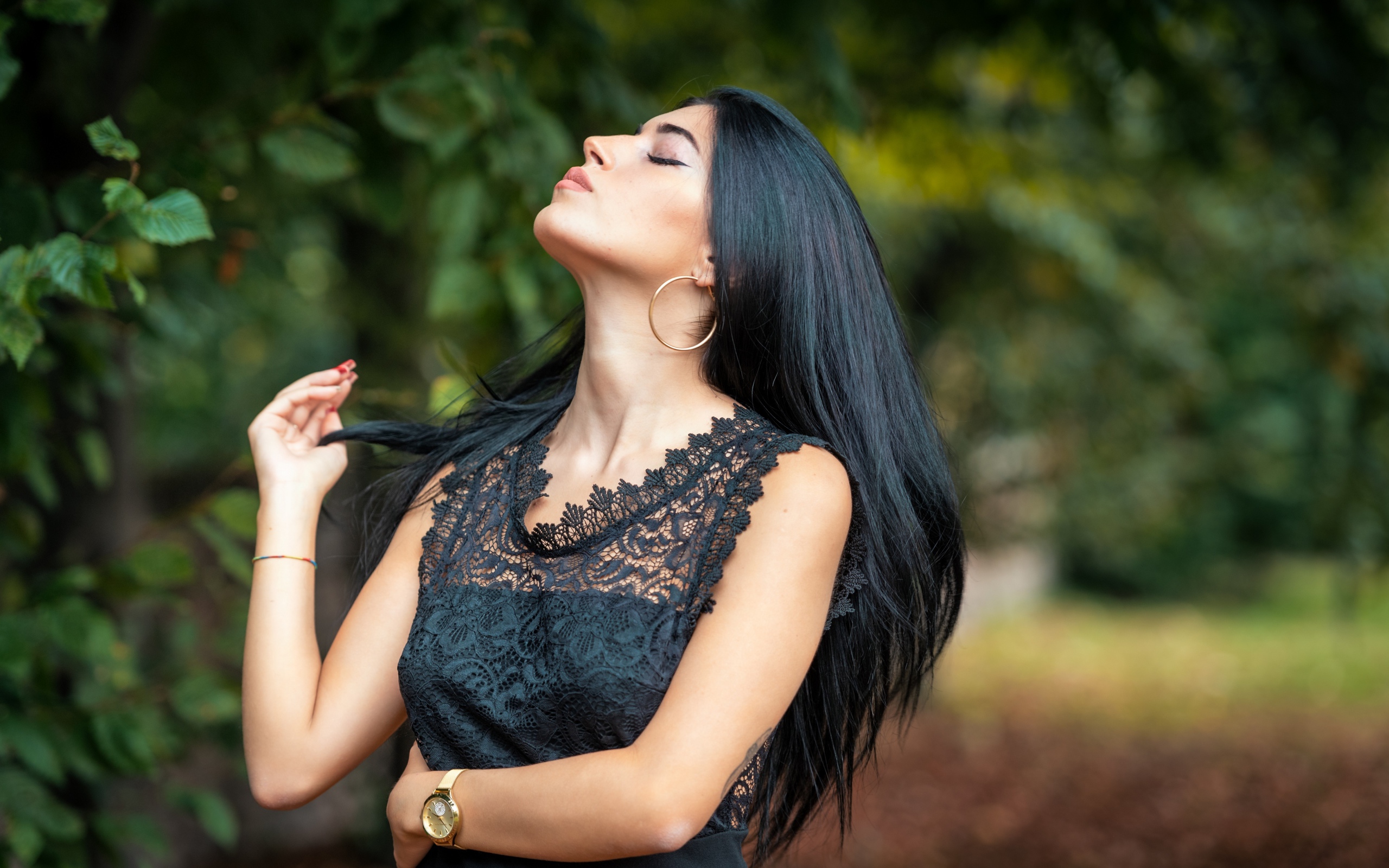 Красивая брюнетка в черном платье с закрытыми глазами в парке