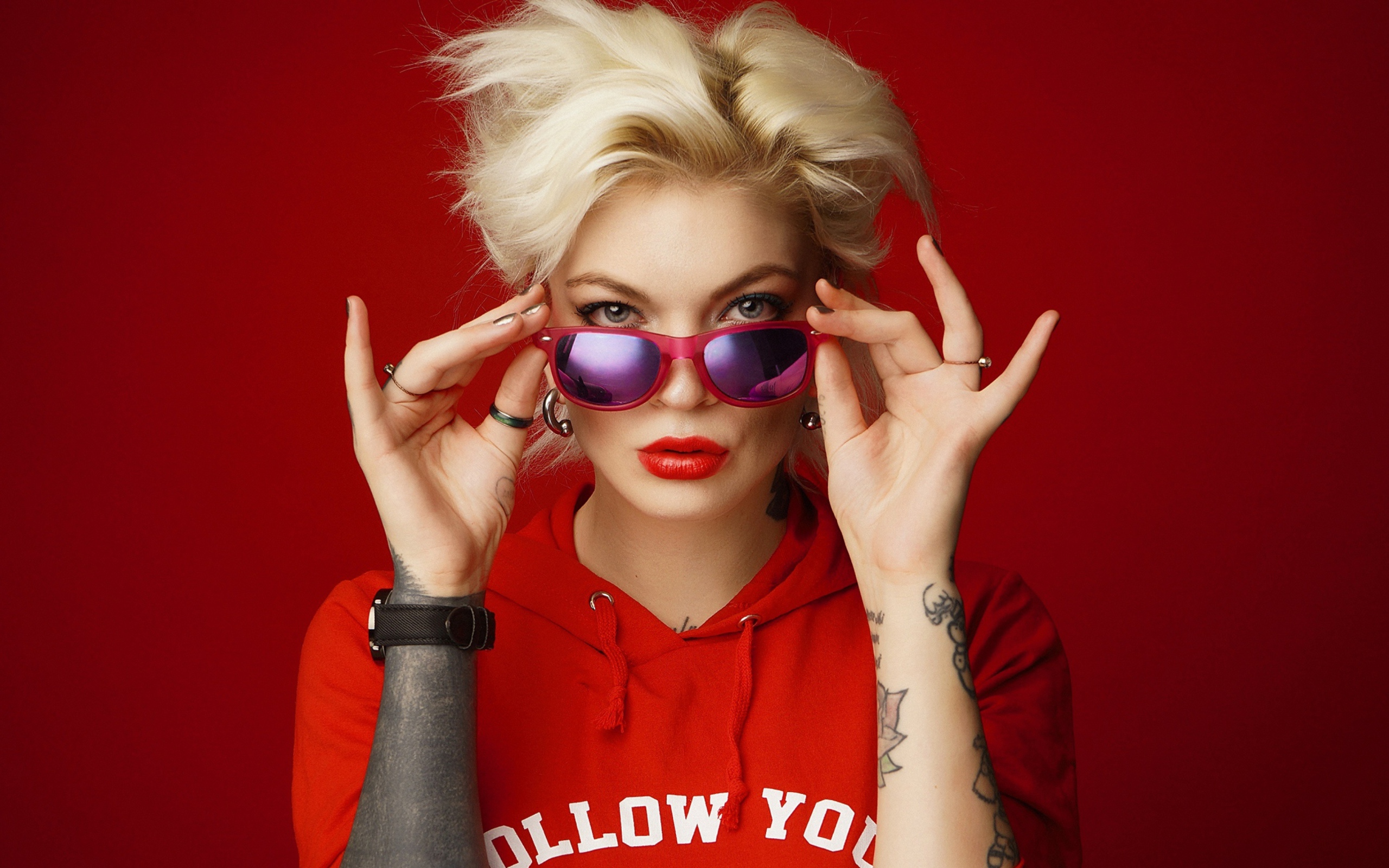 Яркая блондинка с татуировками на руках на красном фоне