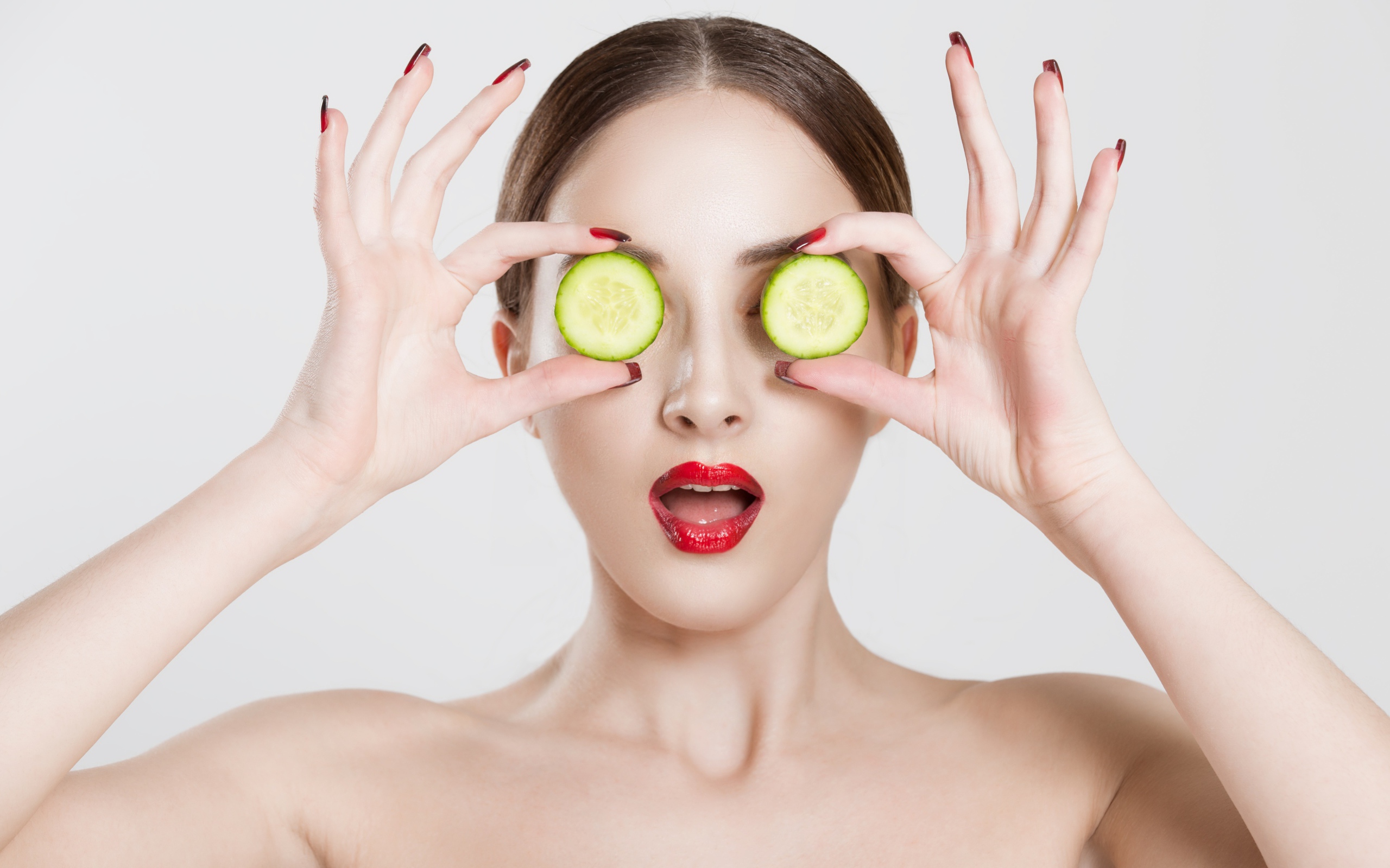 Яркая девушка с огурцами у глаз на сером фоне