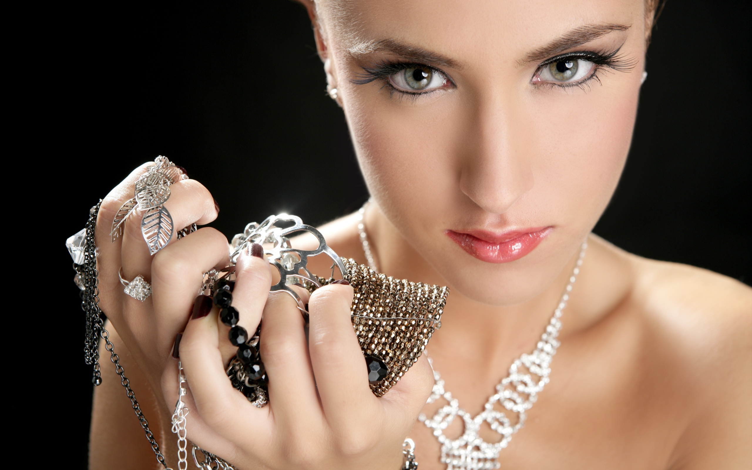 Girl with long eyelashes holds jewelry in her hand.