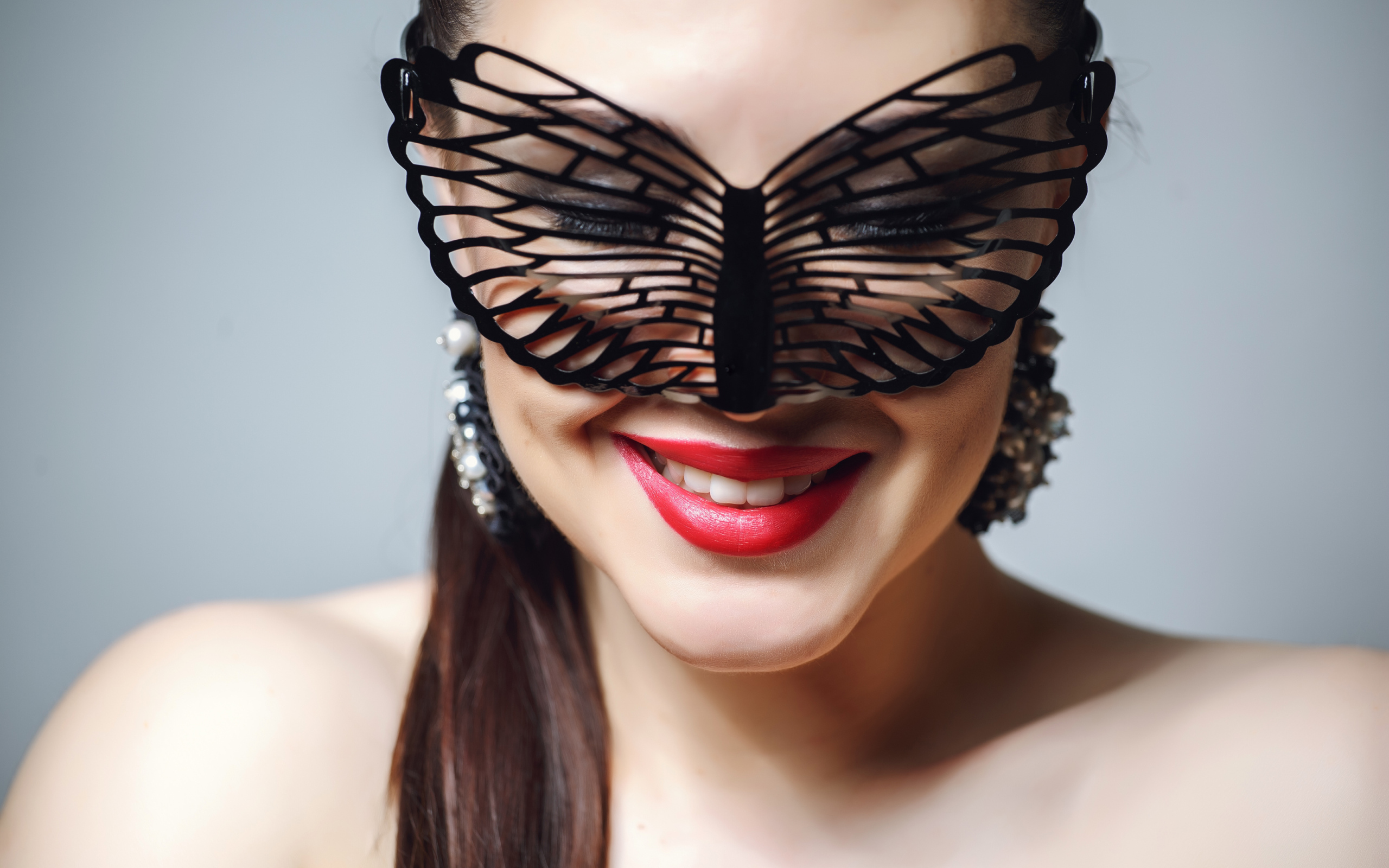 Улыбающаяся девушка в черной маске на сером фоне