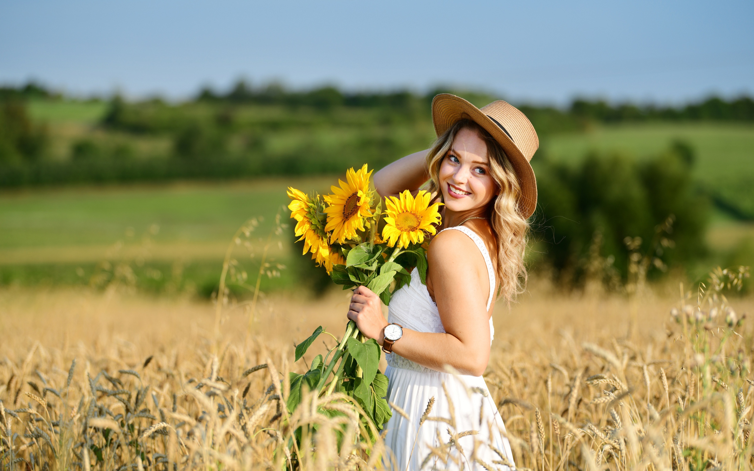 Улыбающаяся девушка на поле с пшеницей с букетом подсолнухов в руке