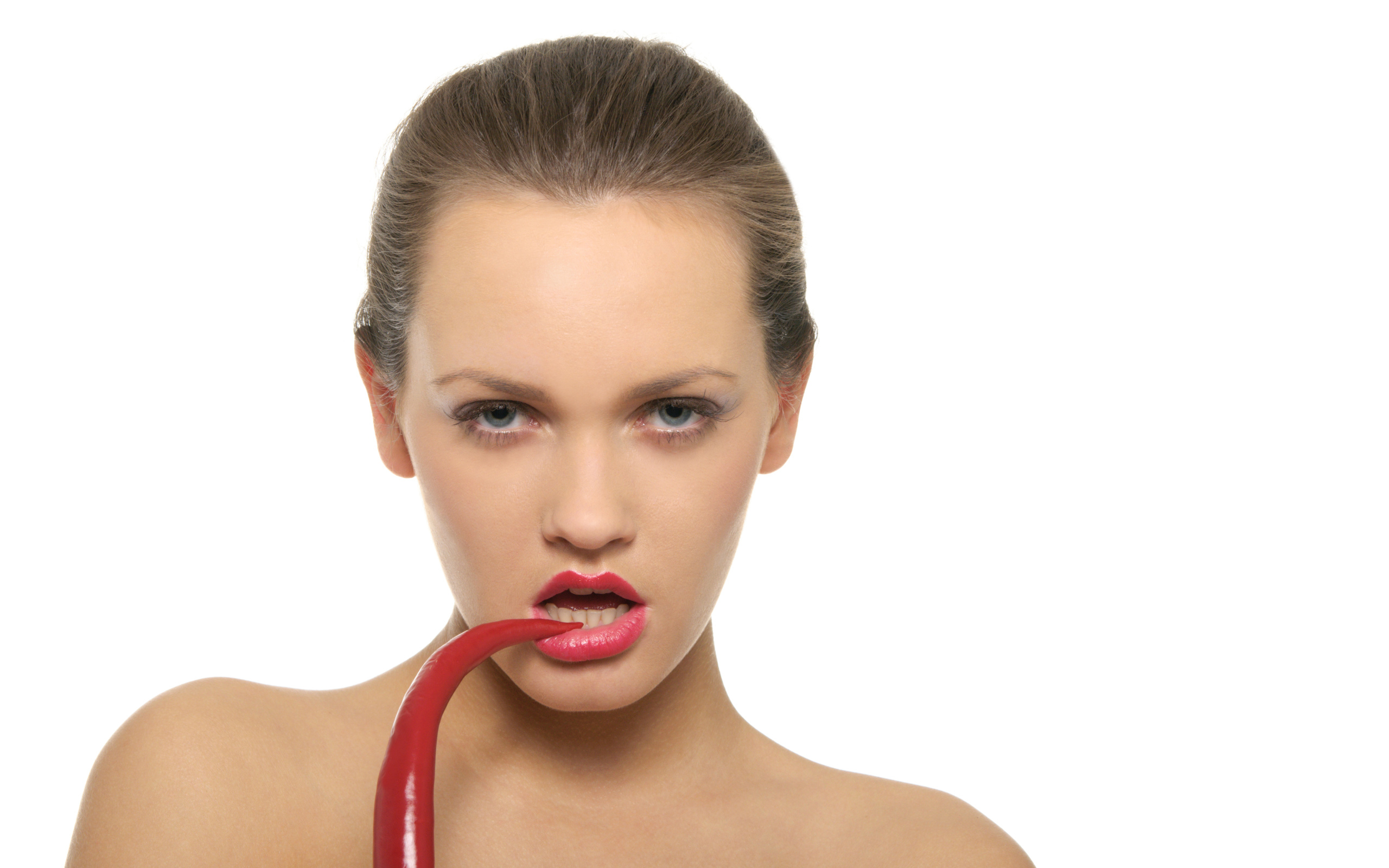 Молодая девушка кусает красный перец на белом фоне