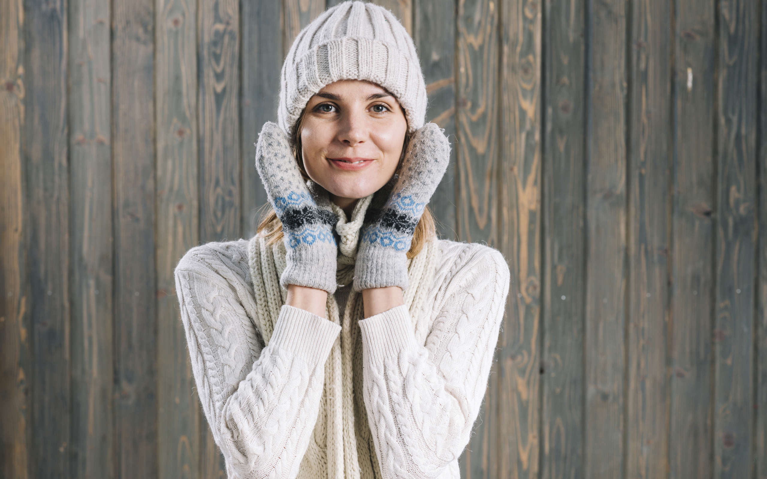 Молодая девушка на шапке, варежках  и теплой шапке на фоне забора