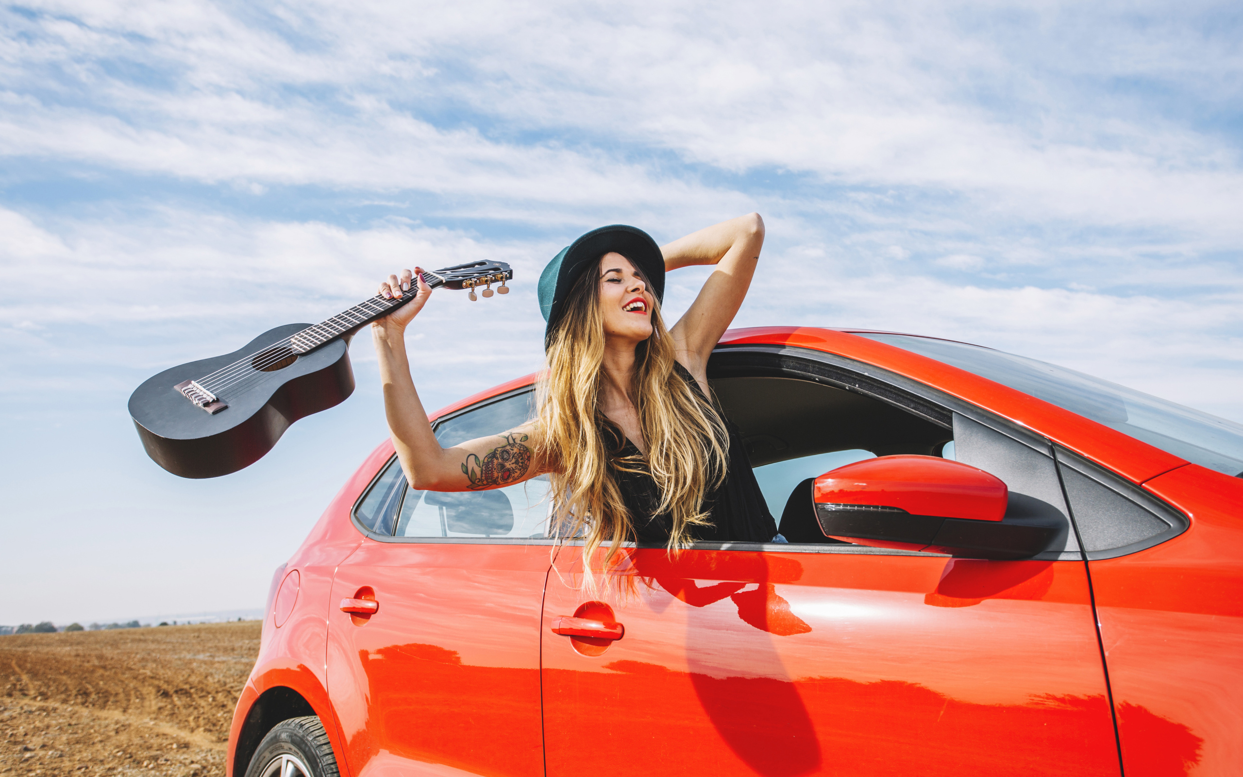 Молодая девушка с гитарой в красной машине летом