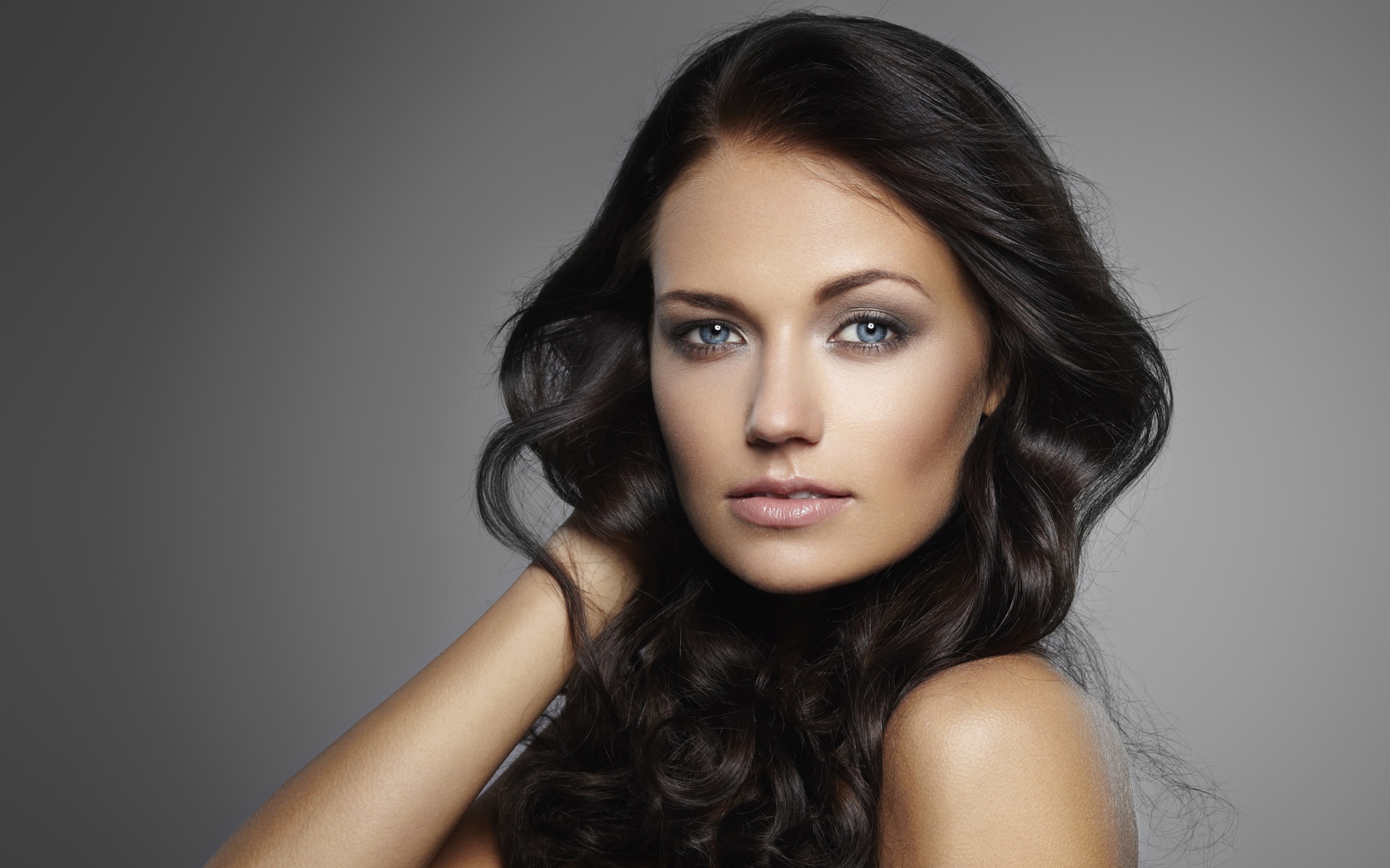 Молодая настоящая голубоглазая длинноволосая брюнетка на сером фоне