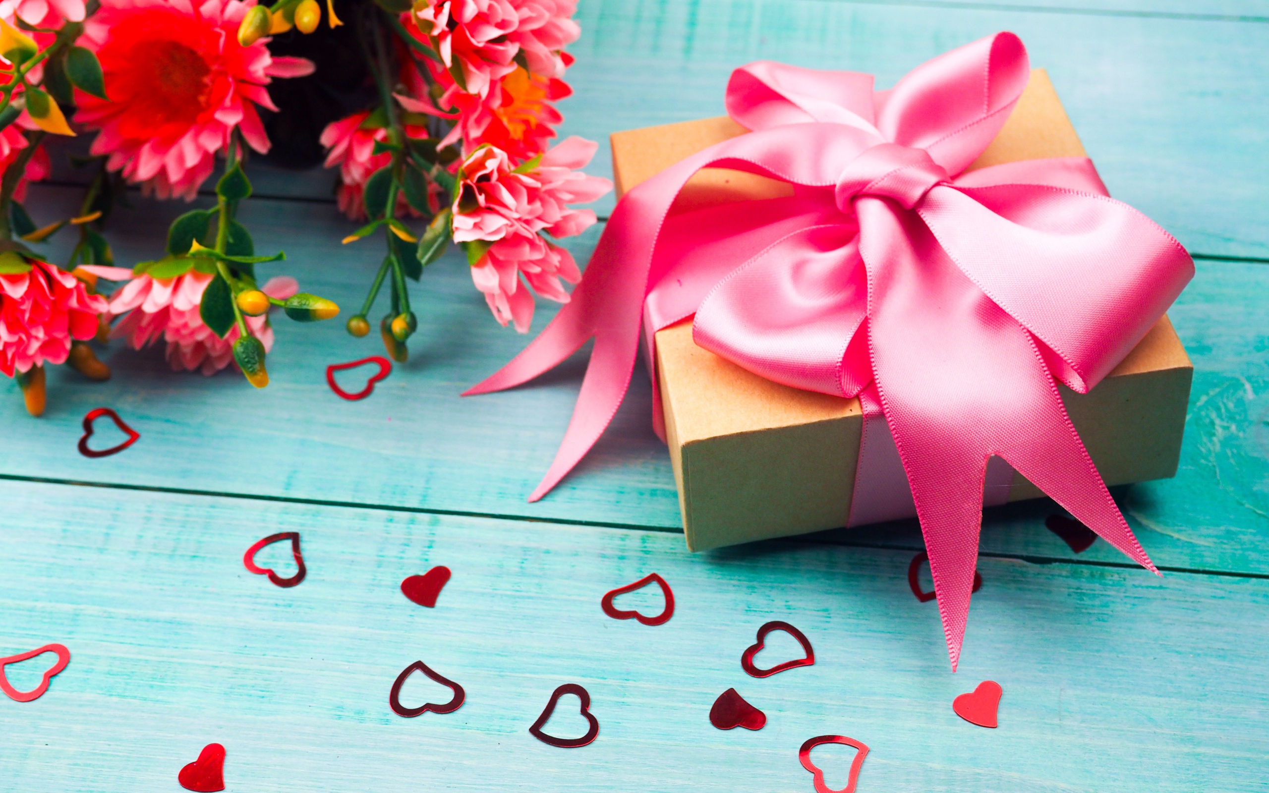 Gift with a pink bow on a blue table with a bouquet