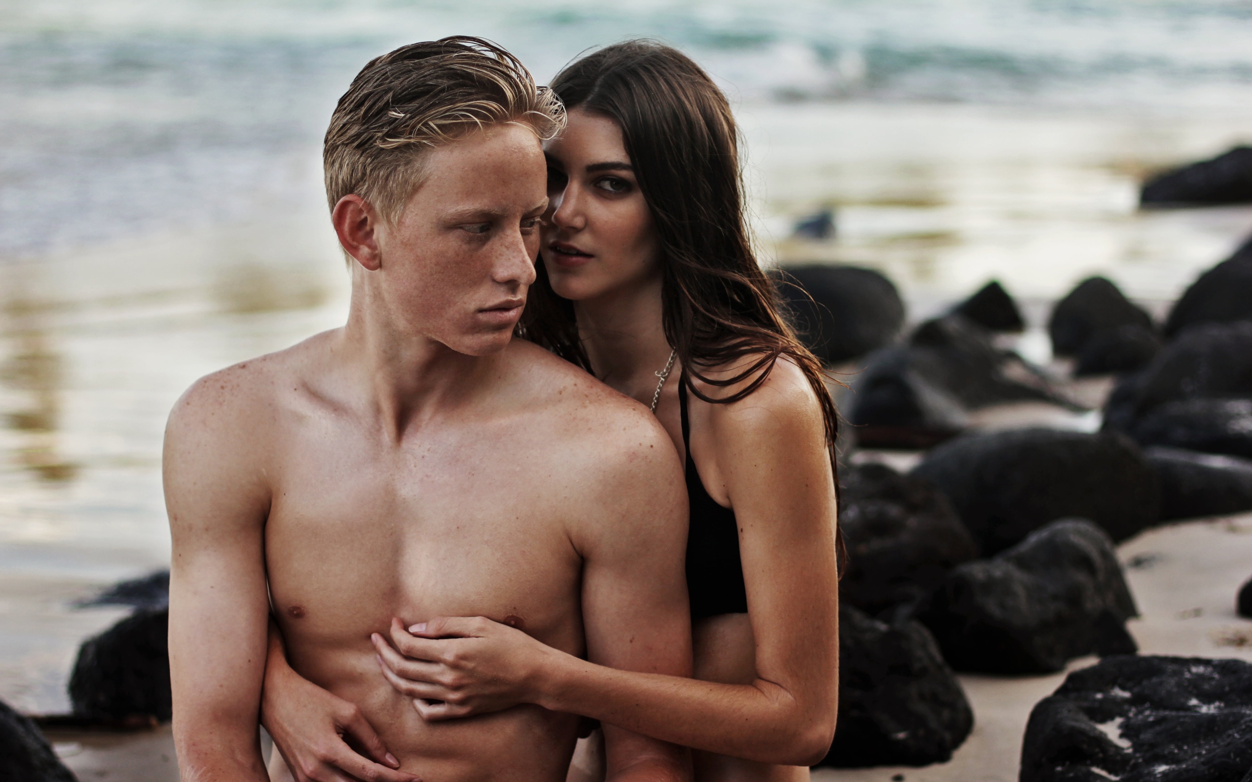 Влюбленная пара сидит на камнях на берегу моря 