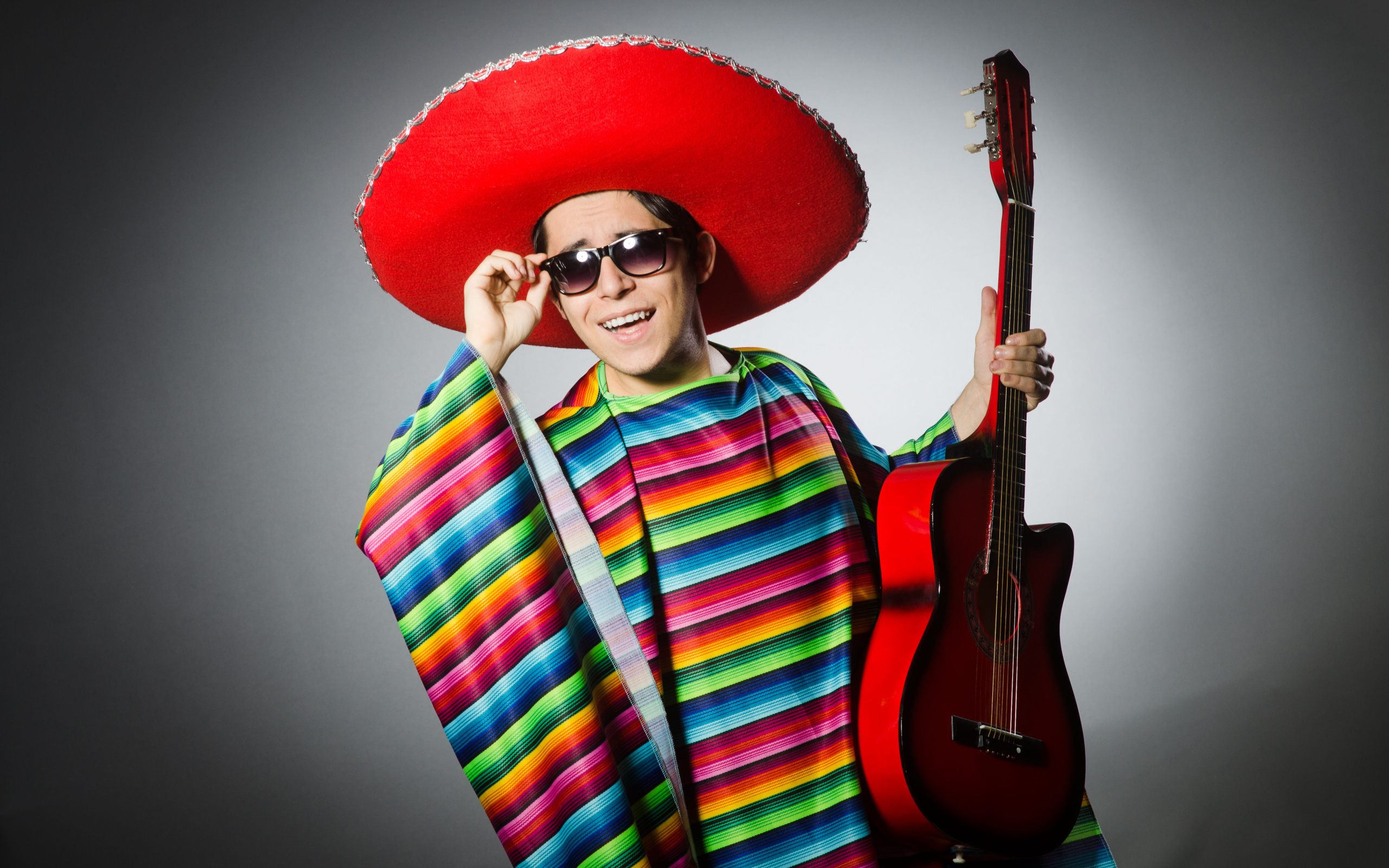 Мужчина в красном сомбреро с гитарой в руках на сером фоне